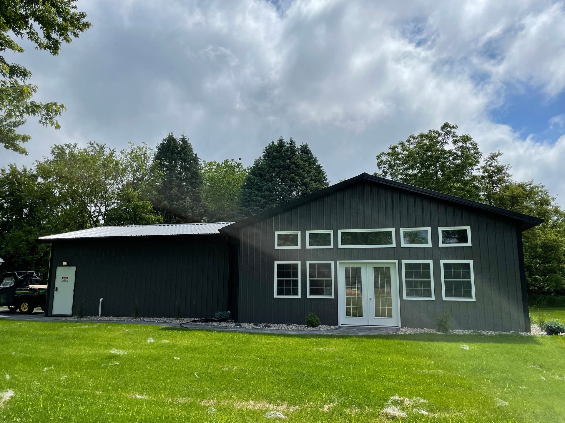 A light gray and black metal building with a stone base, a brown wooden porch, and a black roof.