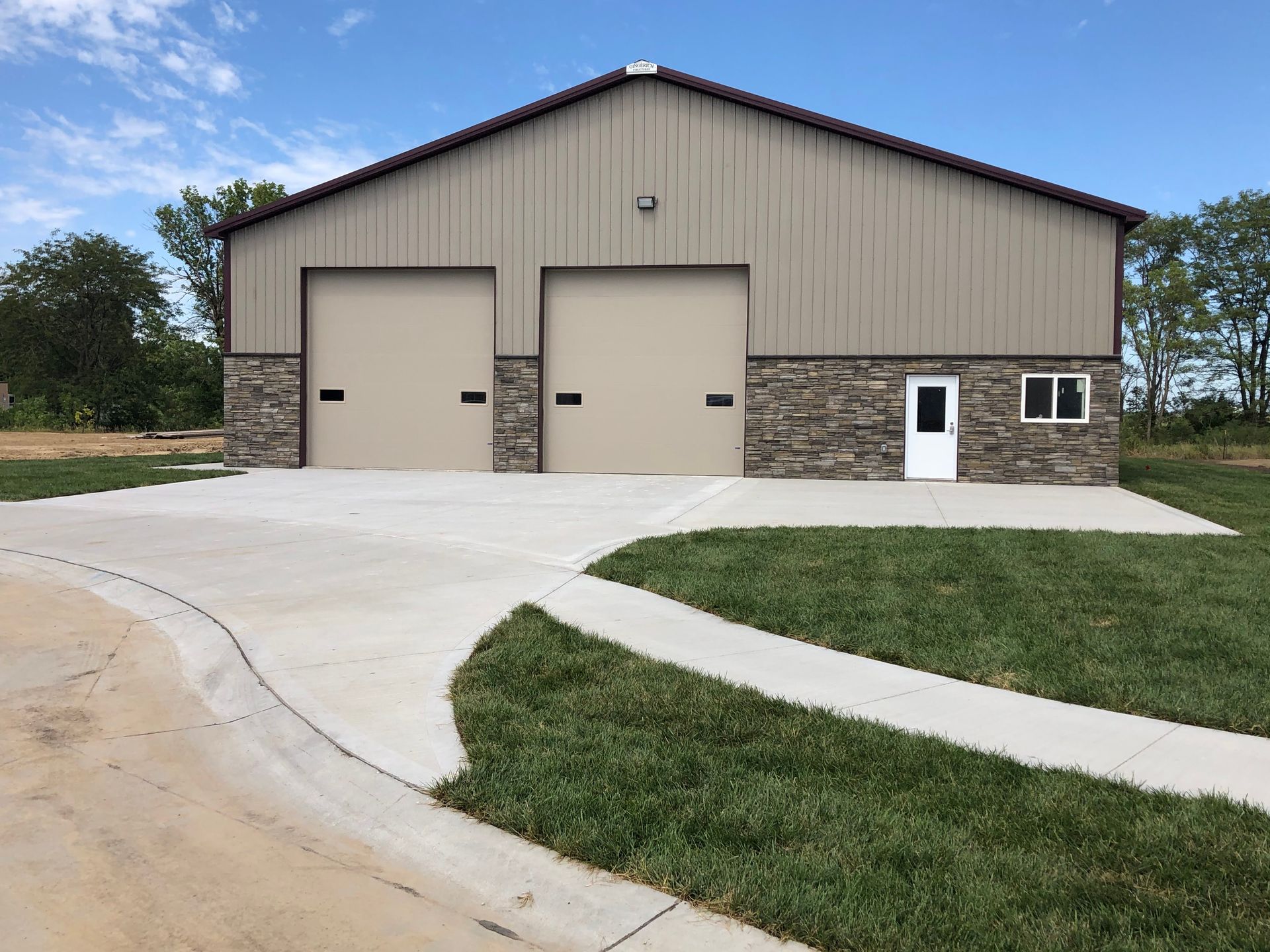 Dark gray barn-style house under construction, with a metal roof and stone accents.