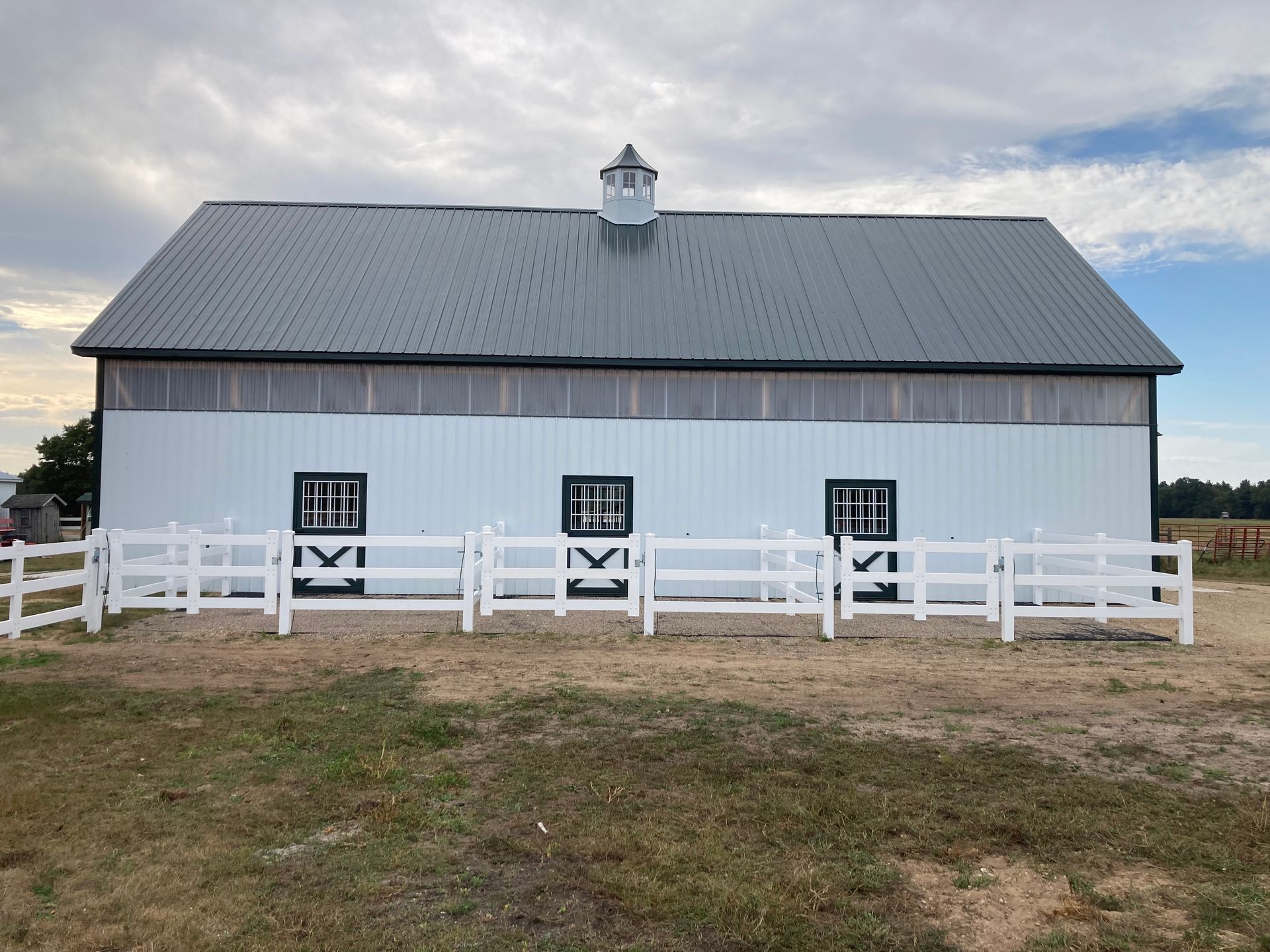 White barn with gray roof, black windows, white fence, under a cloudy sky.