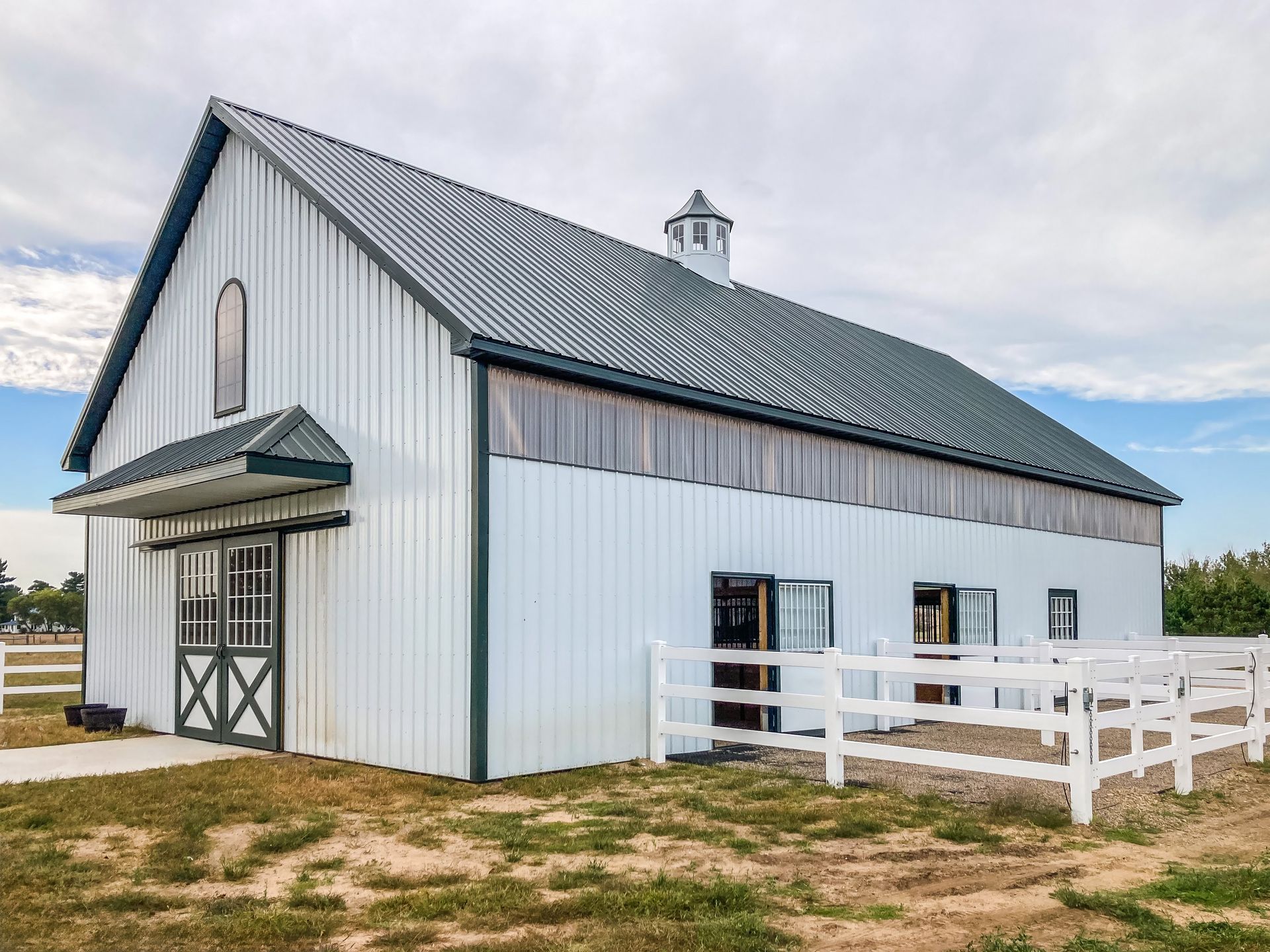 Red and white barn with red roof and small overhang, set on a concrete pad. Two small cupolas. Blue sky.