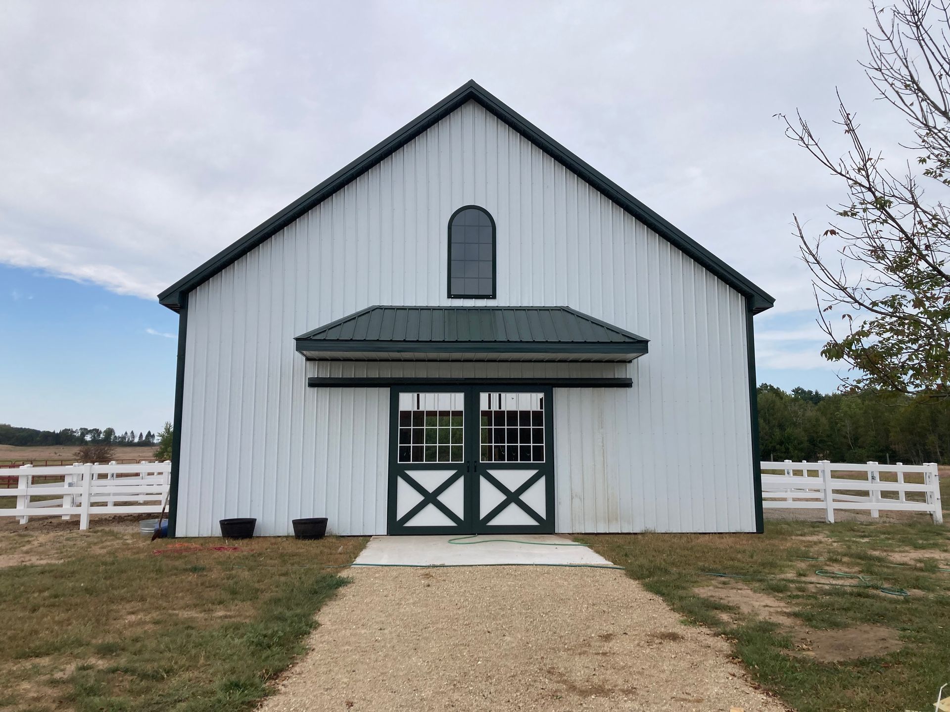 White barn with green trim, arched window, and double doors, pathway leading to entrance, cloudy sky.