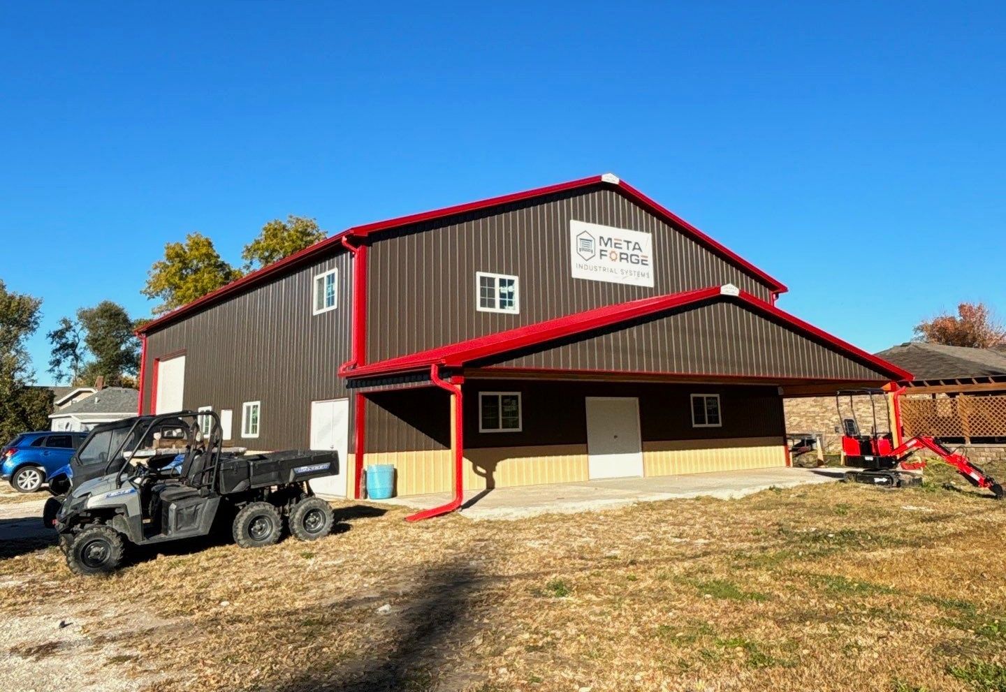 Red barn-style building with red trim, parked ATVs, and a grassy lot under a clear sky