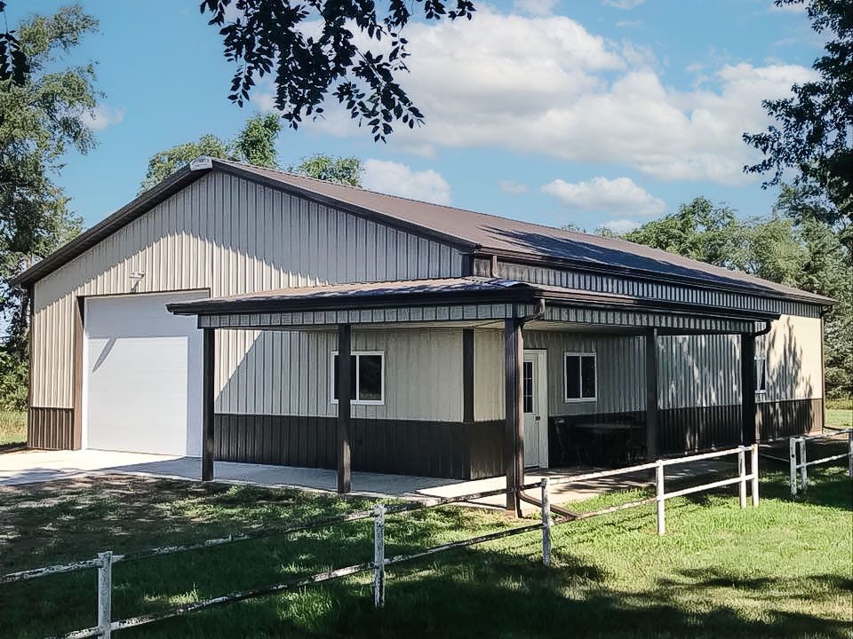 A metal-sided barn with a brown roof and awning. Light and dark brown siding, a white garage door, and green grass.