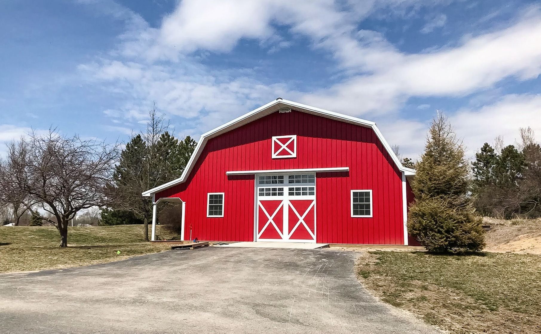 Red barn with white trim and doors, blue sky, and grassy landscape.