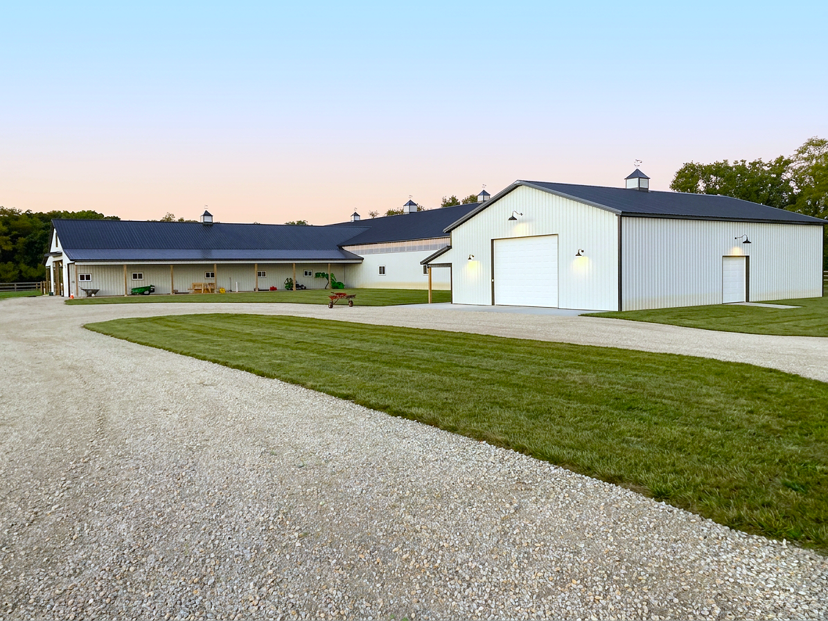 White post-frame building with dark roof and cupola on a rural property