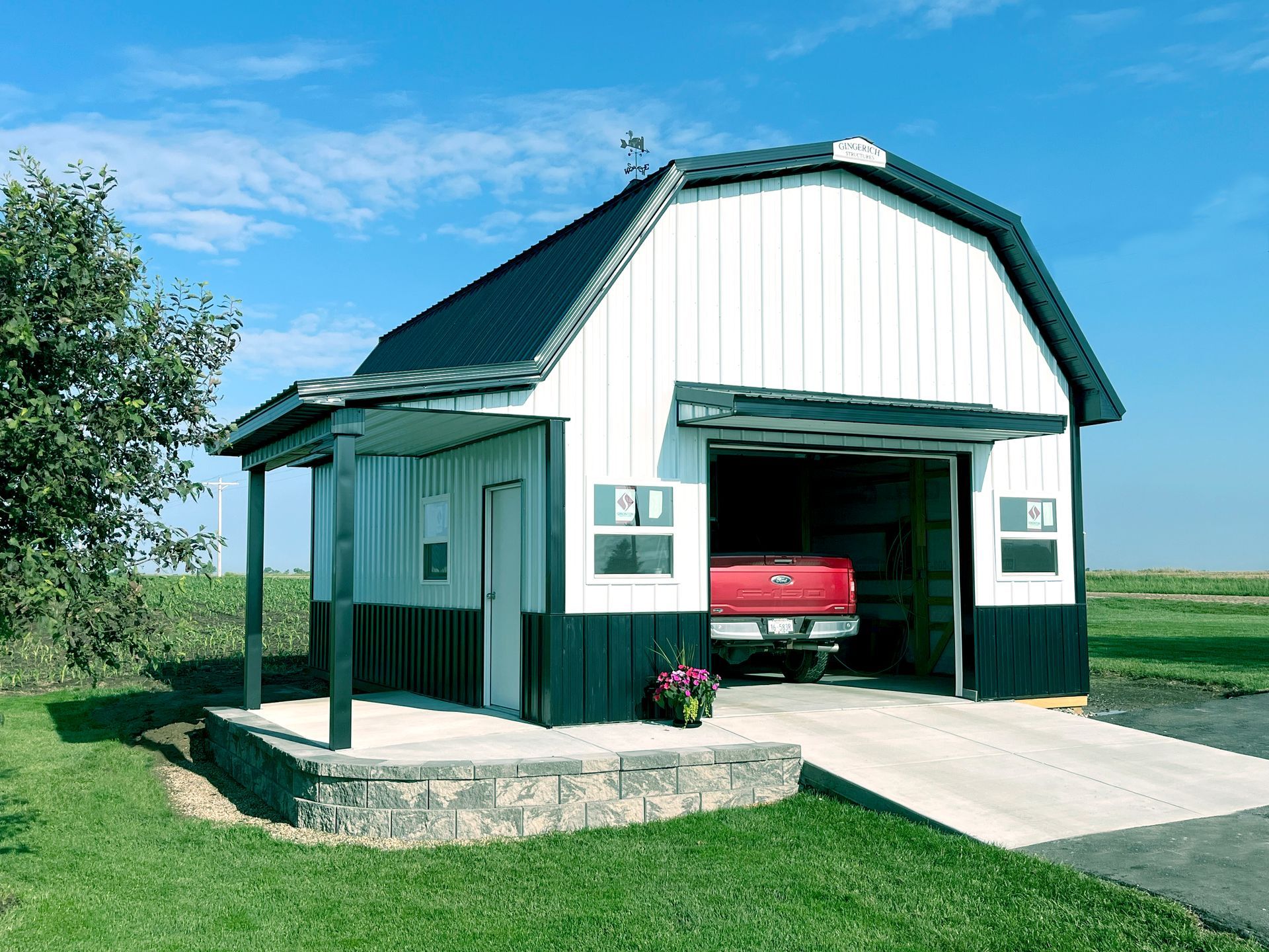 Barn-style garage with a red truck inside; white and black exterior, ramp, porch, and a blue sky.