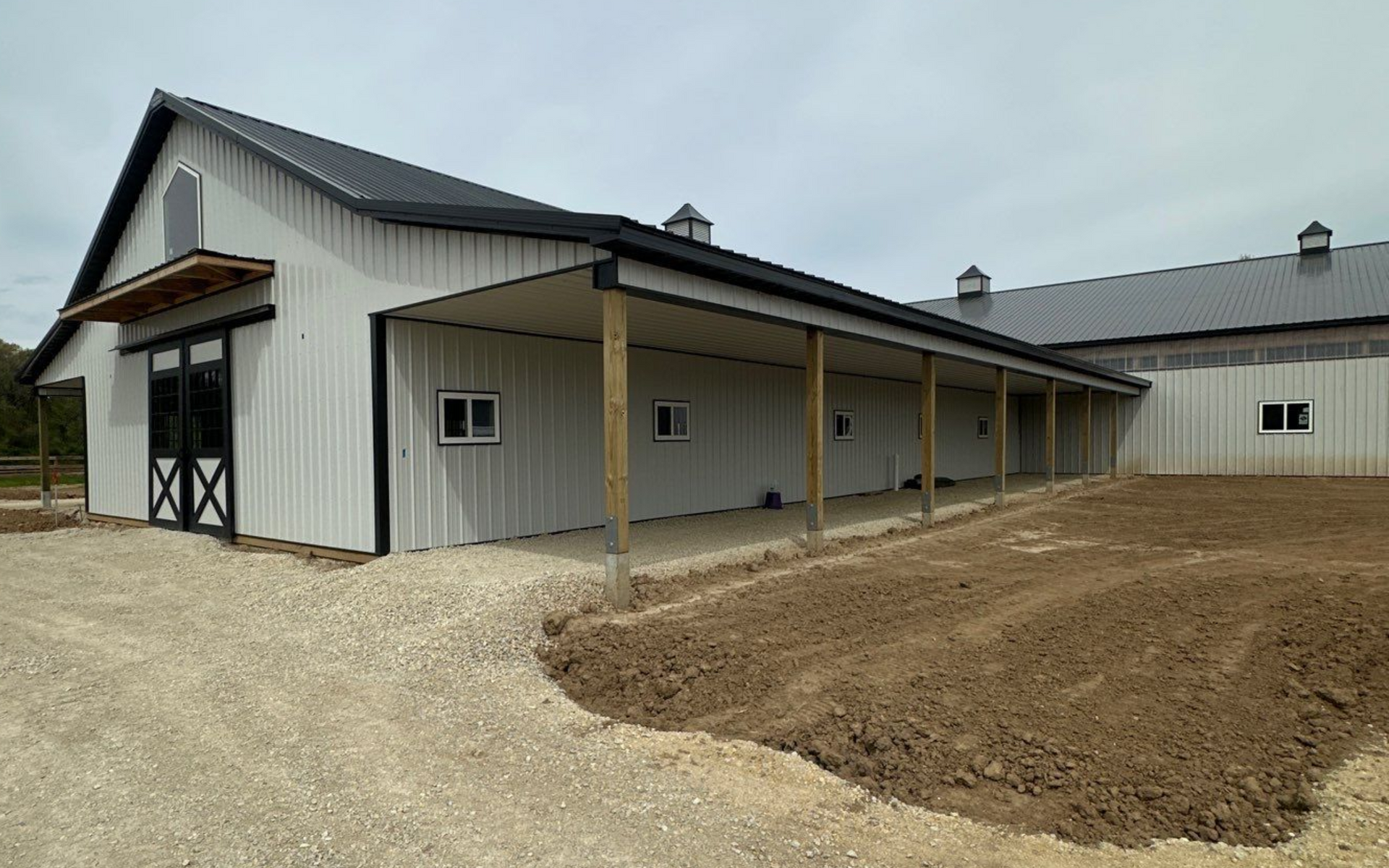A white metal building with three garage doors and a brown roof under a blue sky.