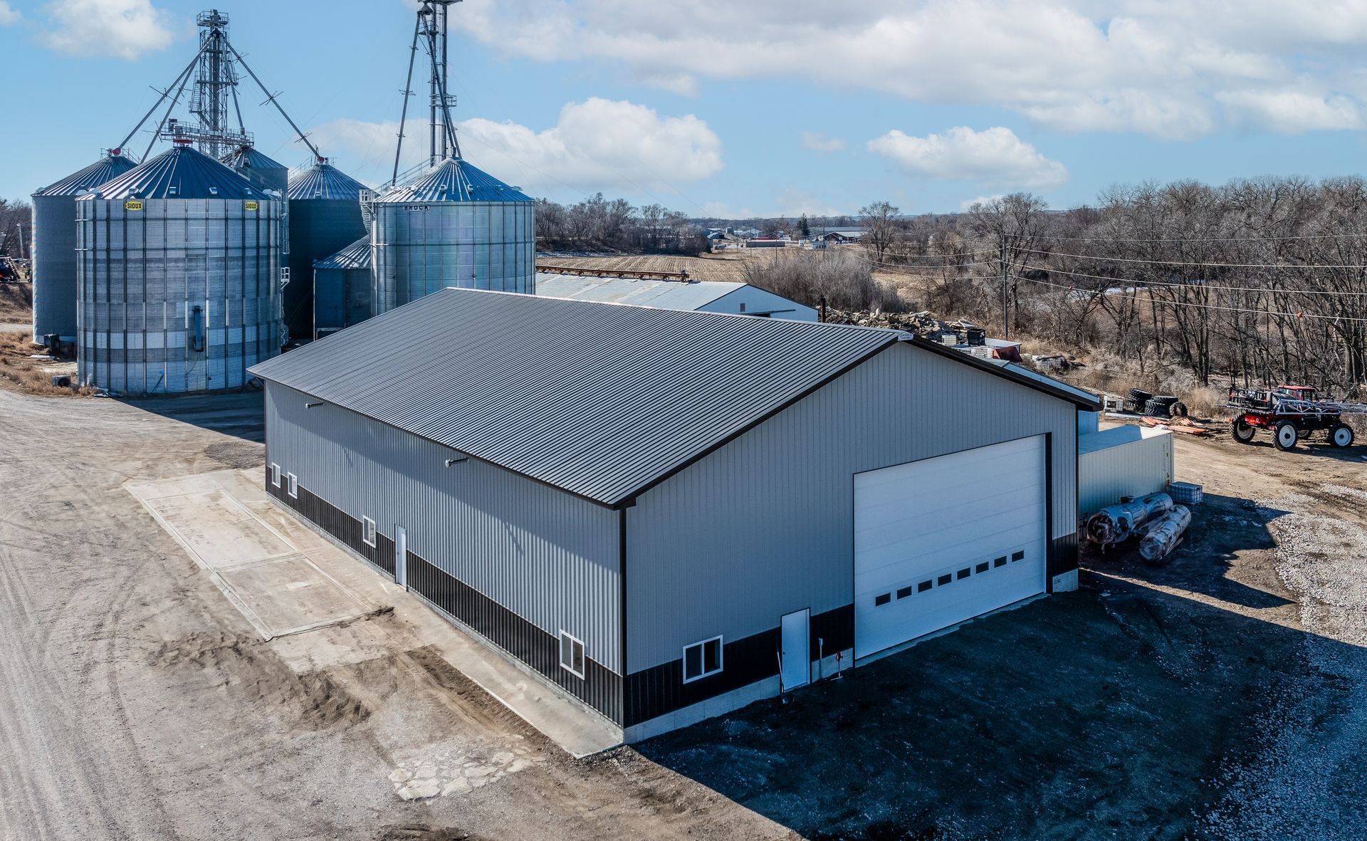 A metal building with a large garage door, silos in the background, rural setting.