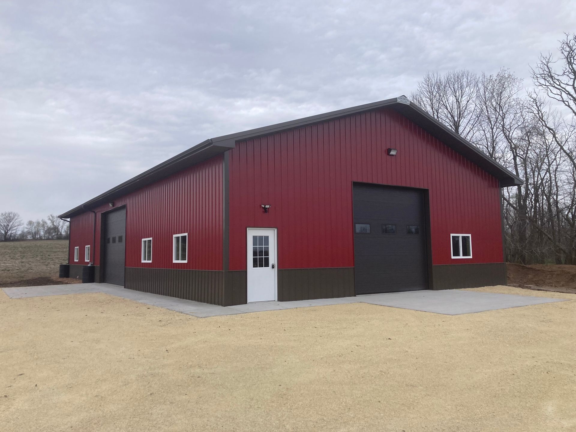 Metal barn with a brown roof and a covered porch on a grassy lot.