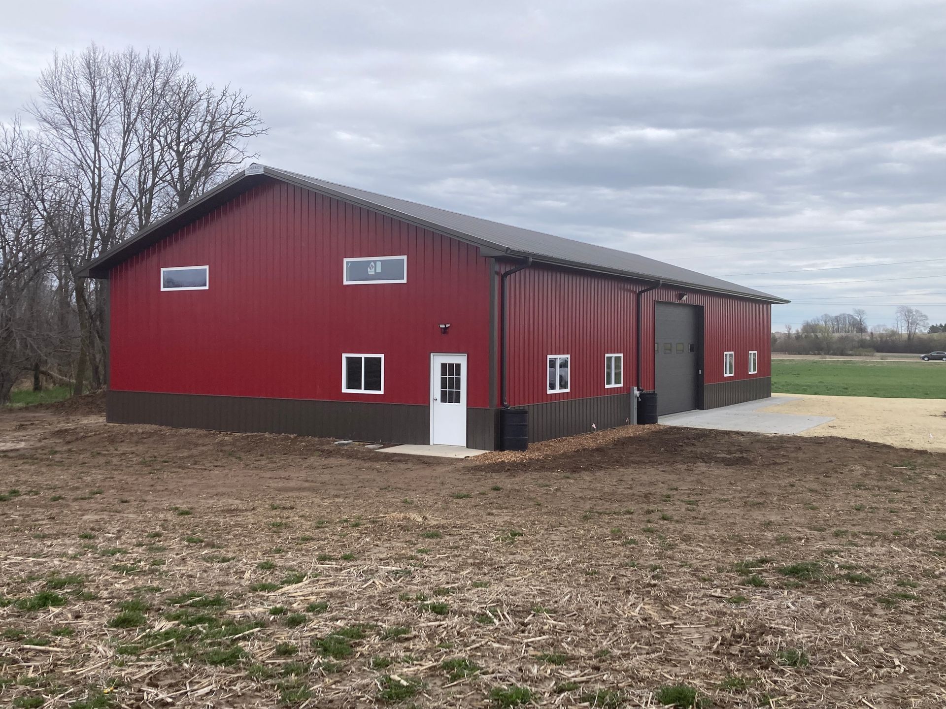 Red and brown metal building with a dark roof, windows, and a large garage door on a cloudy day.