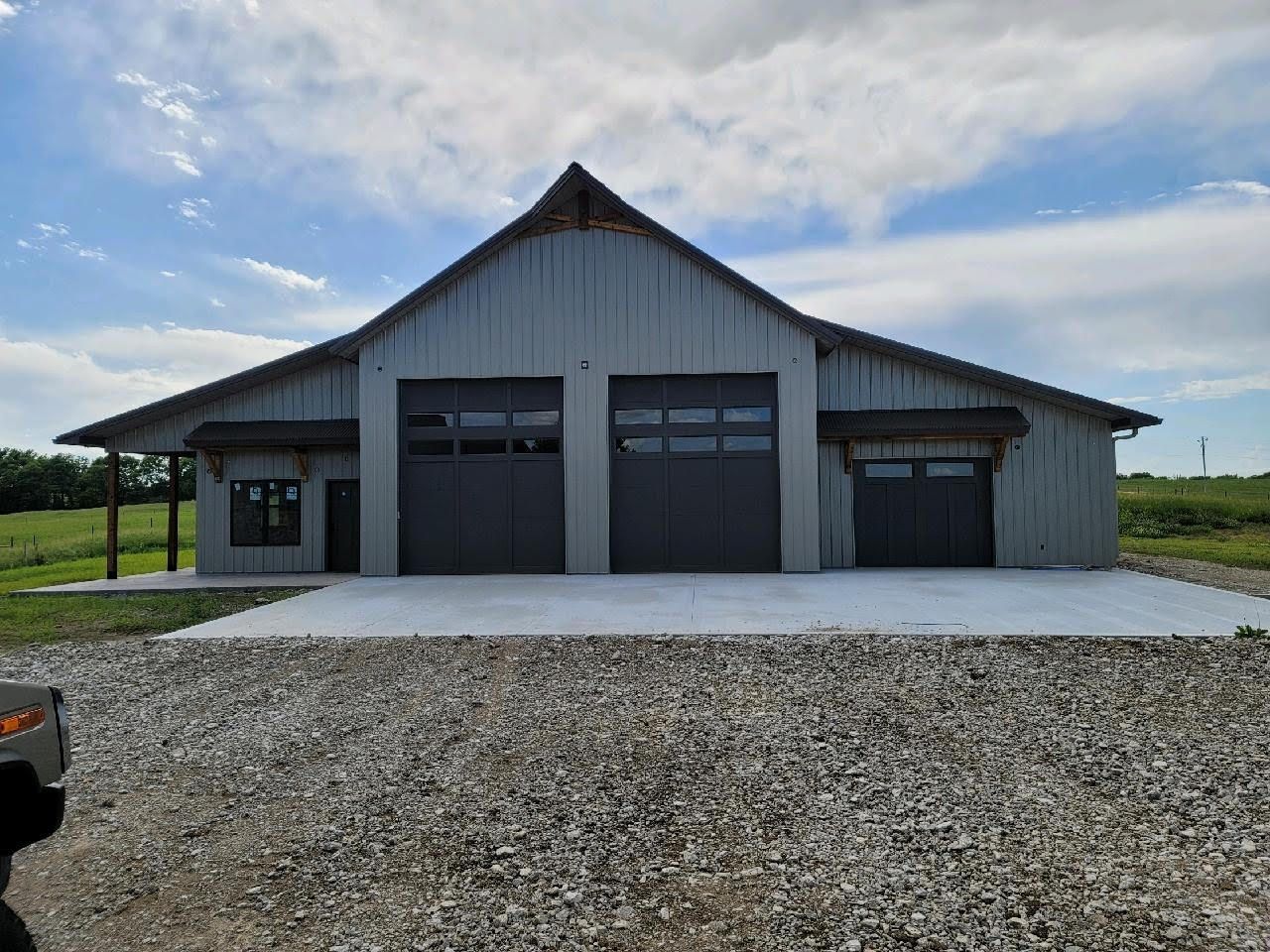 Red and brown metal building with a dark roof, windows, and a large garage door on a cloudy day.
