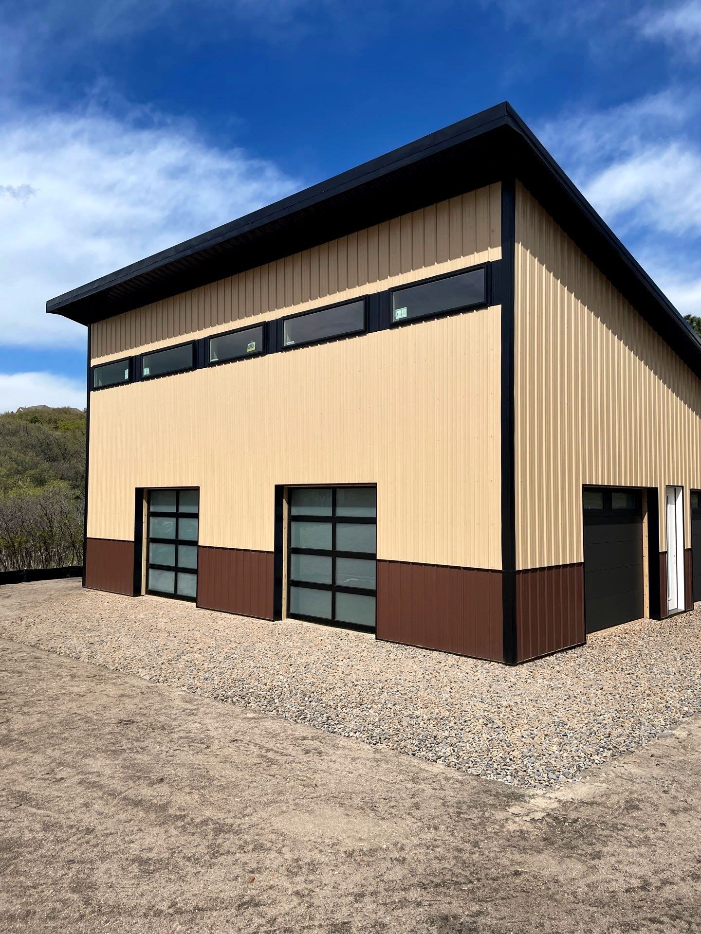 Tan and brown metal warehouse building with large garage doors on a gravel lot under a blue sky