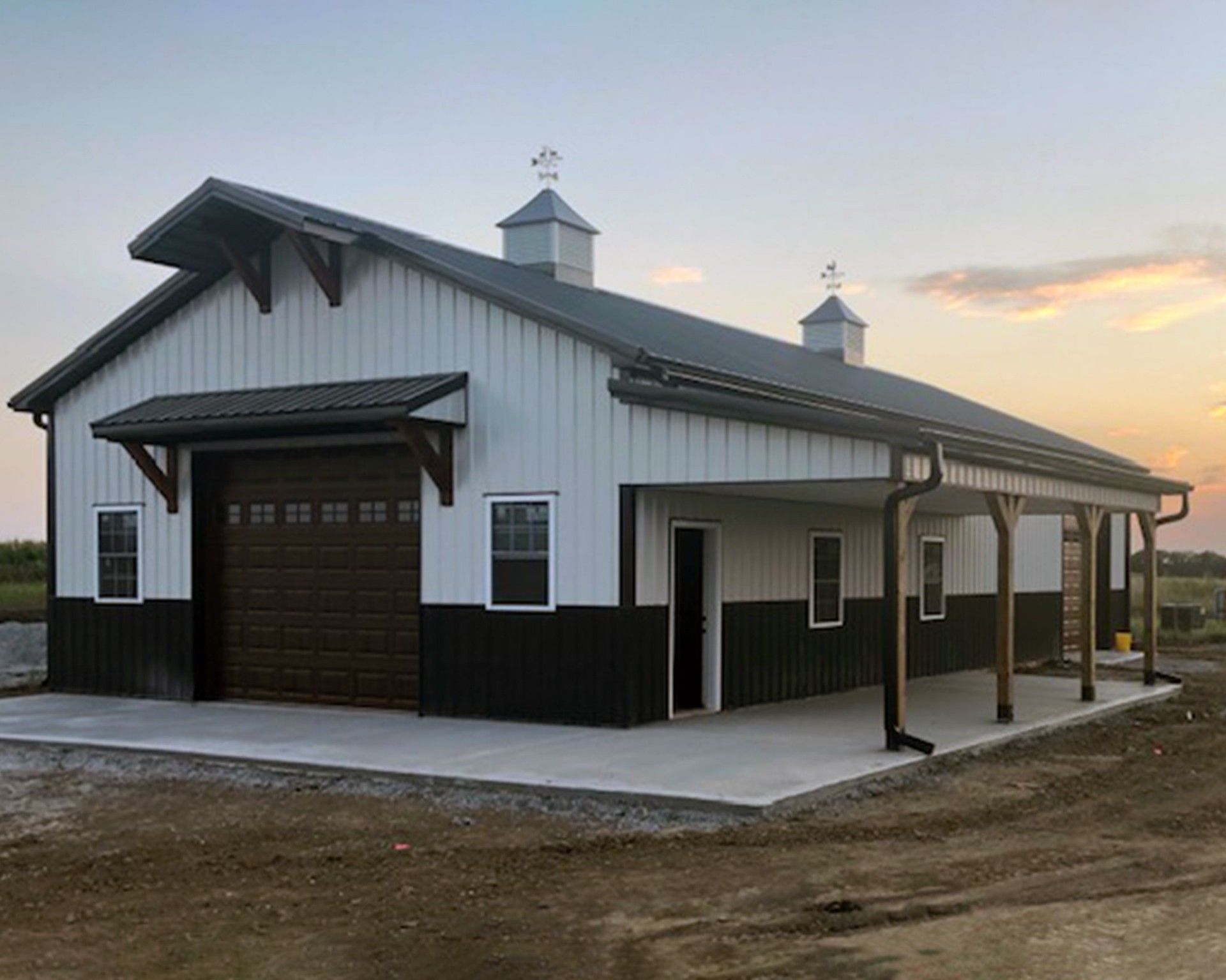 Metal building with red trim, two windows, and open door. Grassy area with gravel driveway.