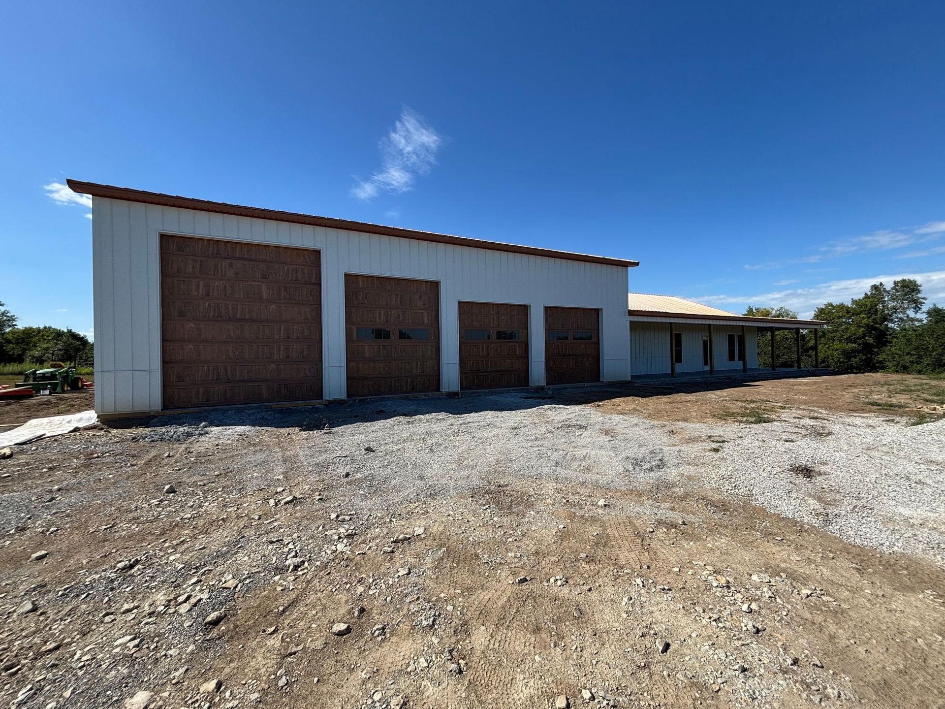 A white metal building with three garage doors and a brown roof under a blue sky.