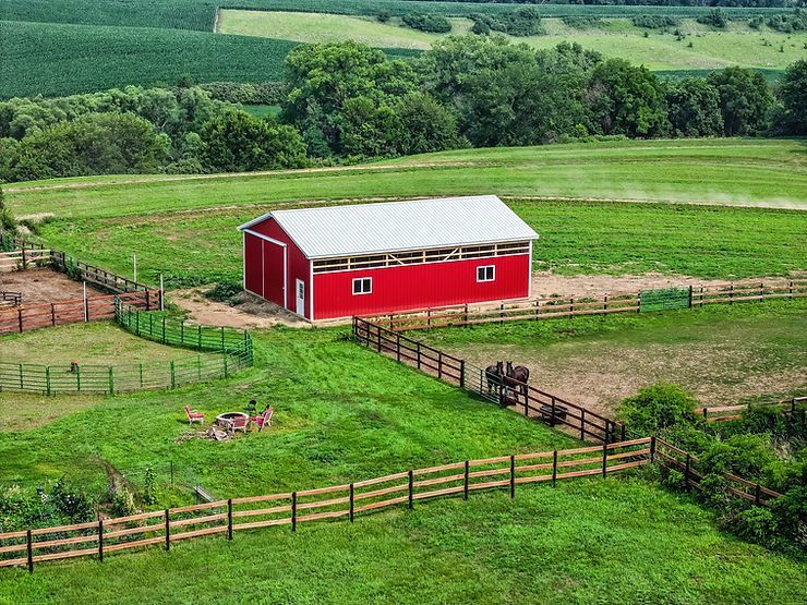 Red barn on a green farm surrounded by fences, in a rural setting.