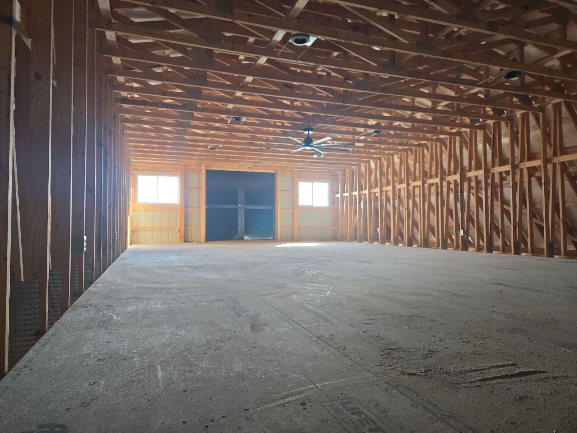 Wide view of a spacious, unfinished building interior with wooden wall studs, exposed ceiling trusses, and concrete floors.
