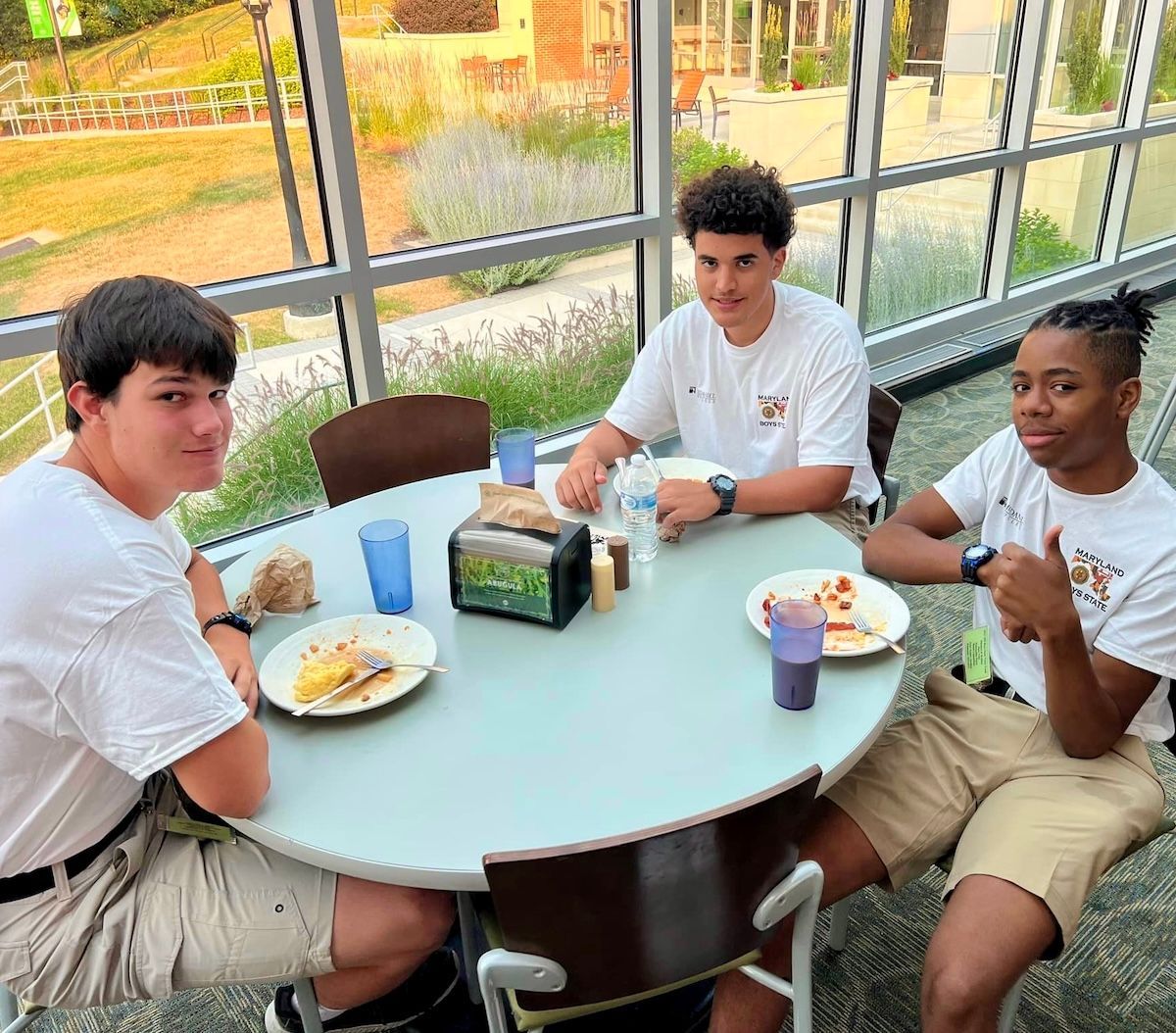 Three young men are sitting at a table with plates of food and drinks