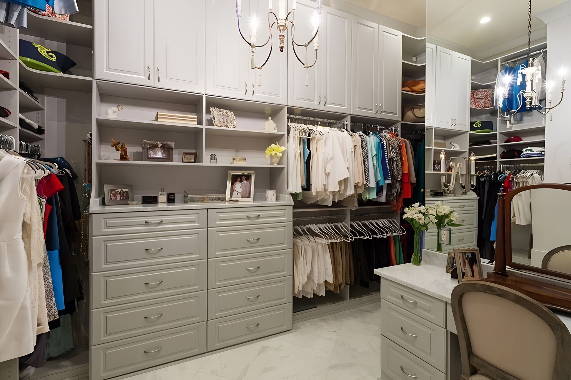 Elegant walk-in closet with white cabinetry, hanging clothes, drawers, and a vanity chair
