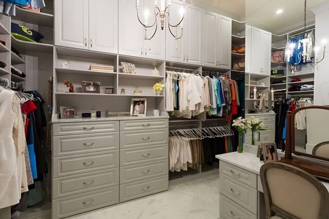 Walk-in closet with white cabinets, drawers, hanging clothes, and a vanity chair