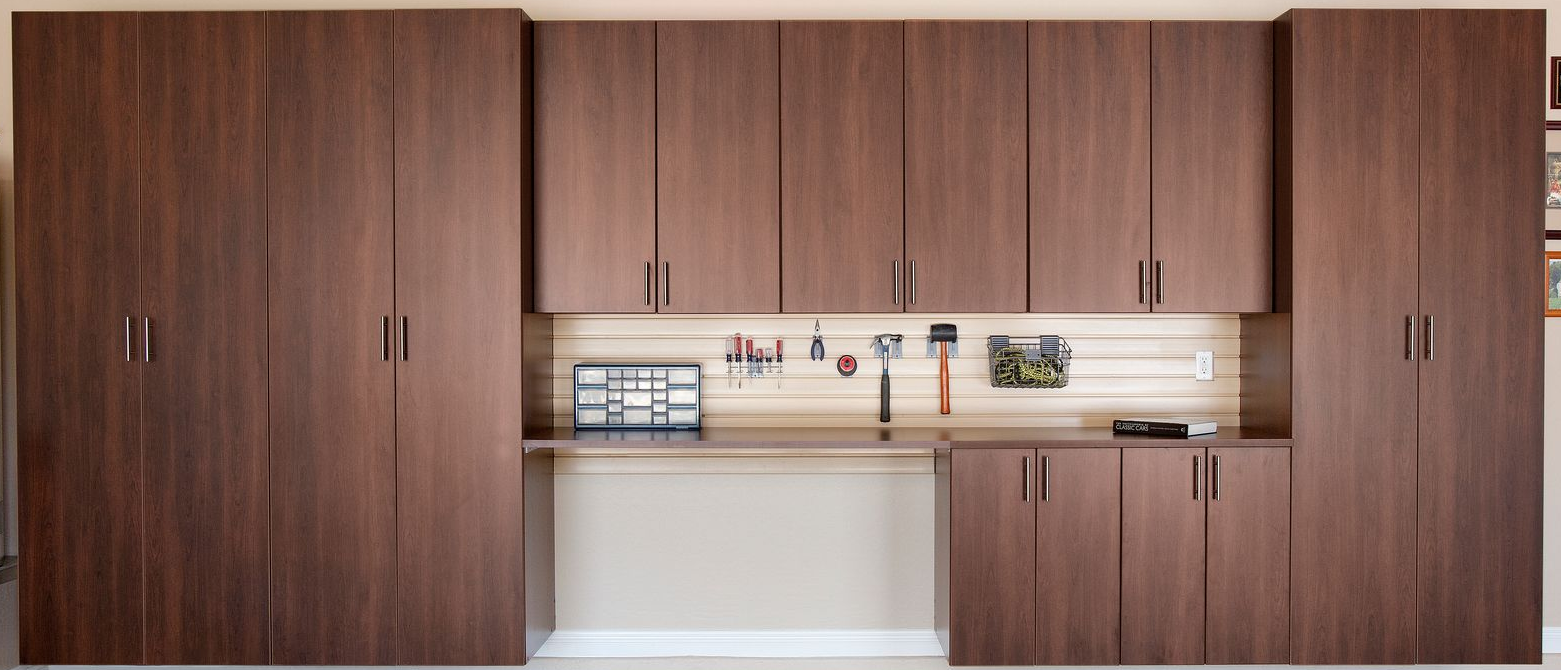 Brown garage cabinets with a work bench and tool hanging rack.