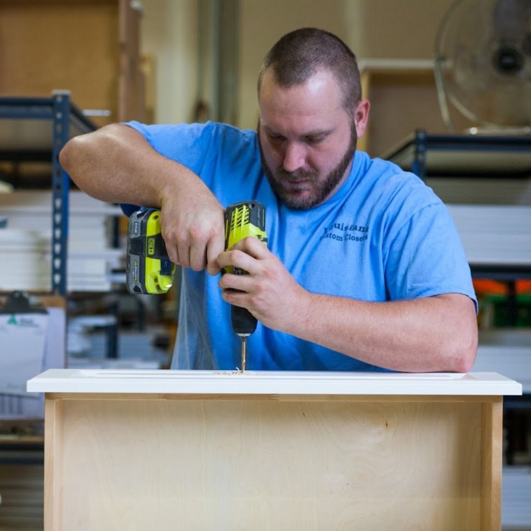 Man using a drill on a wooden drawer in a workshop.