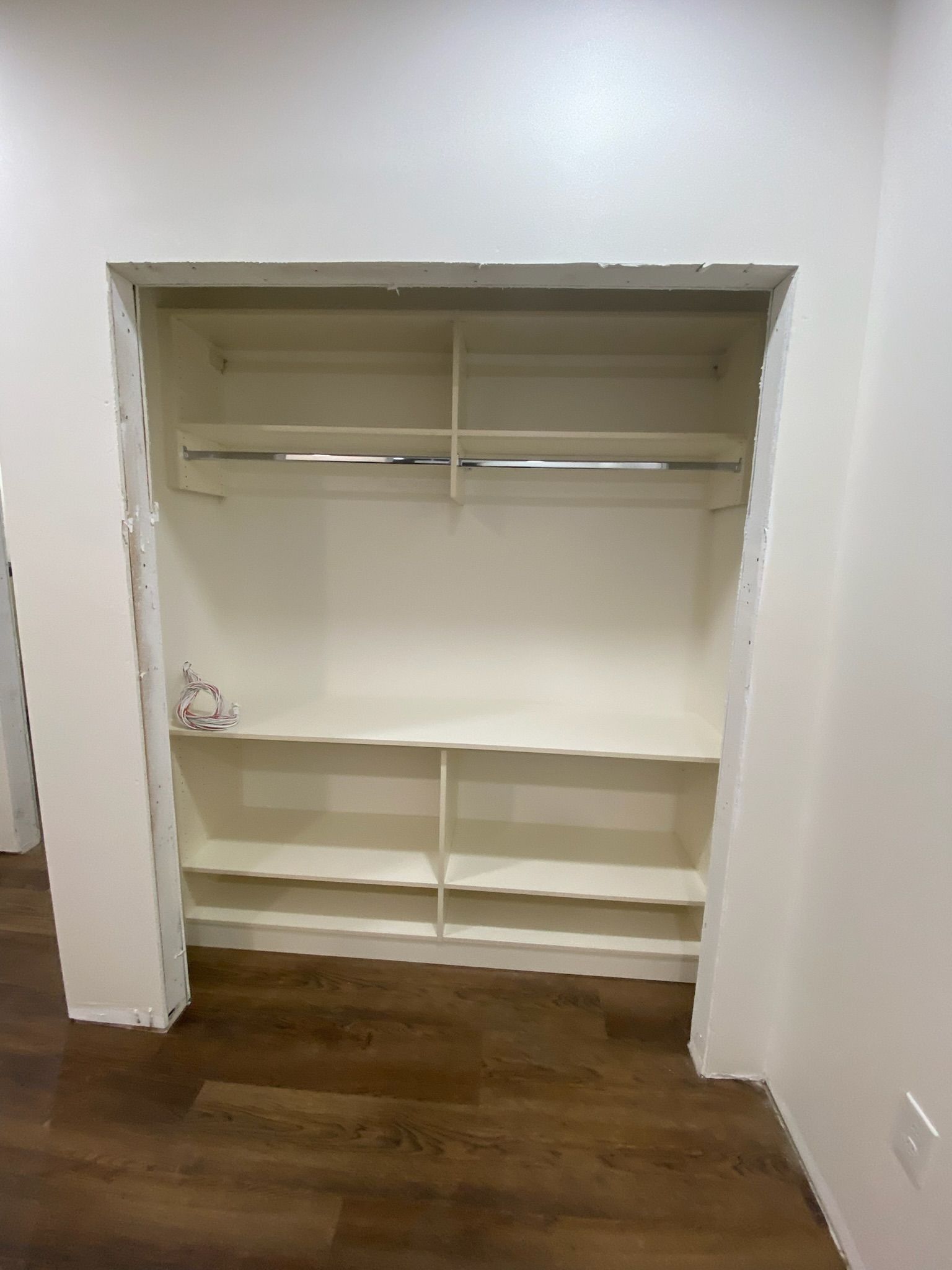 Empty closet with shelves and a hanging rod. White walls, wood floor.