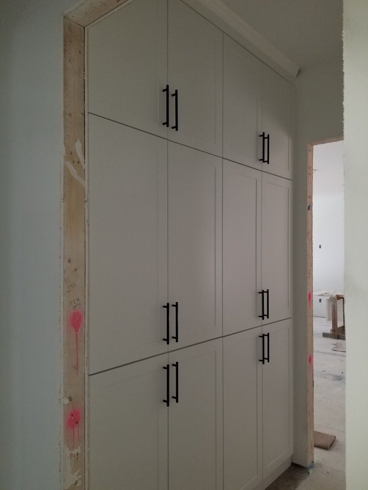 White built-in storage cabinets with black handles in a doorway. Construction setting.