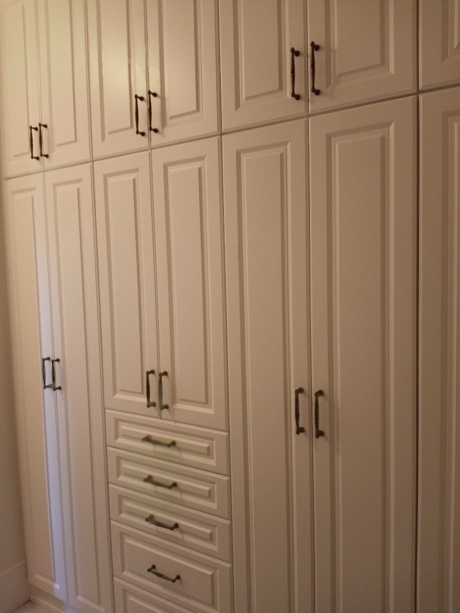 White built-in closet with multiple doors and drawers, dark handles, and a paneled design.
