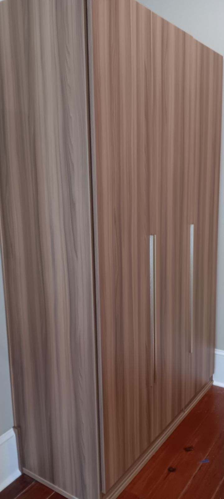 Brown wooden wardrobe with three doors and silver handles on a wooden floor.