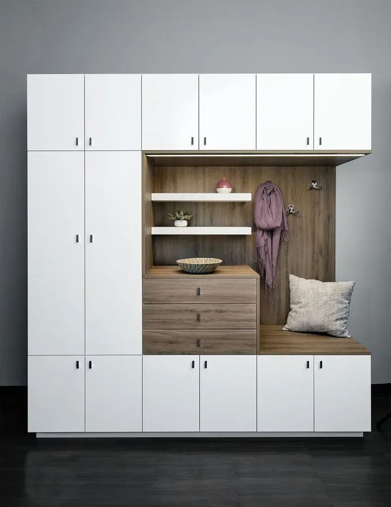 White and wood entryway storage unit with bench, cabinets, drawers, shelves, and hooks against a gray wall.
