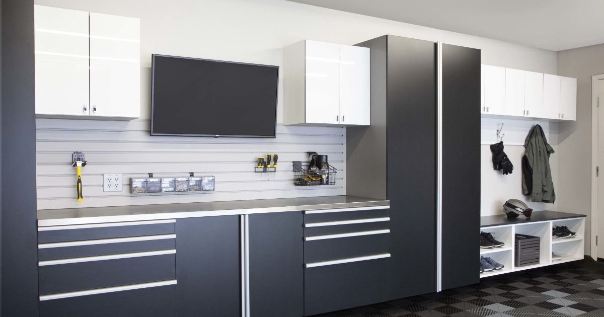 Garage with dark gray and white storage cabinets, workbench, and wall-mounted TV.