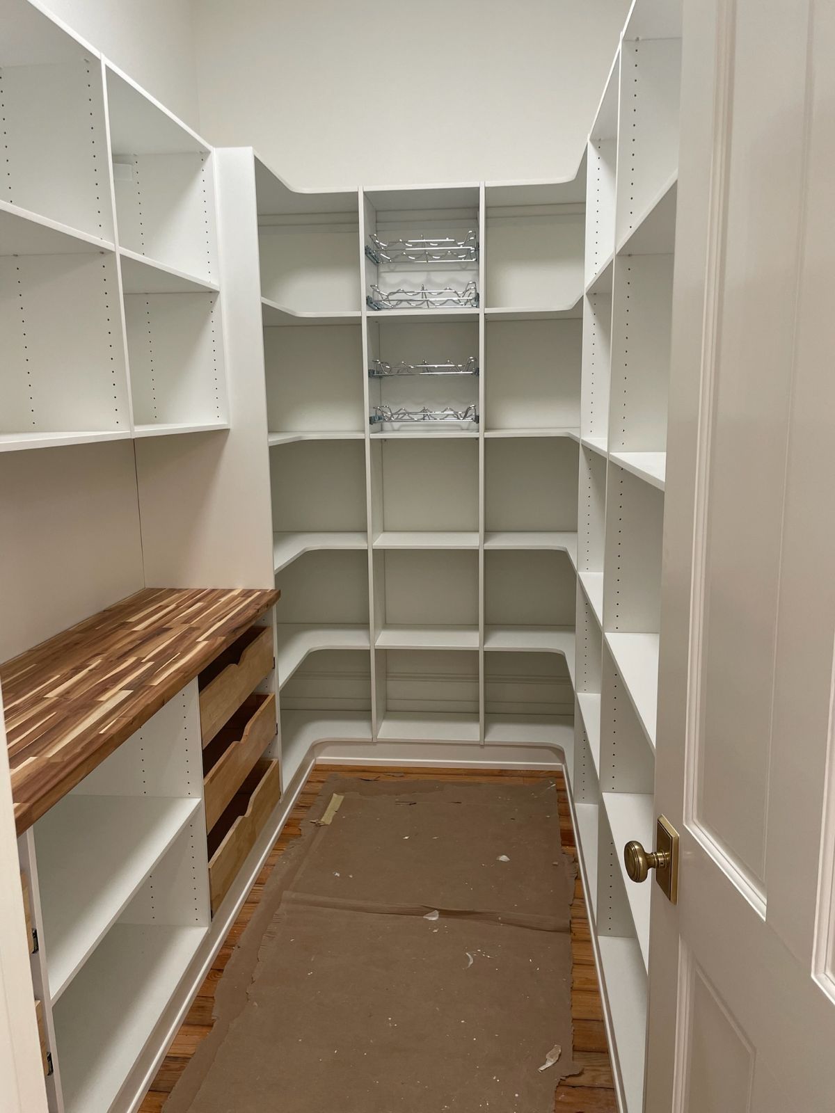 White pantry with built-in shelves and a wooden countertop. Interior view, shelves are empty.