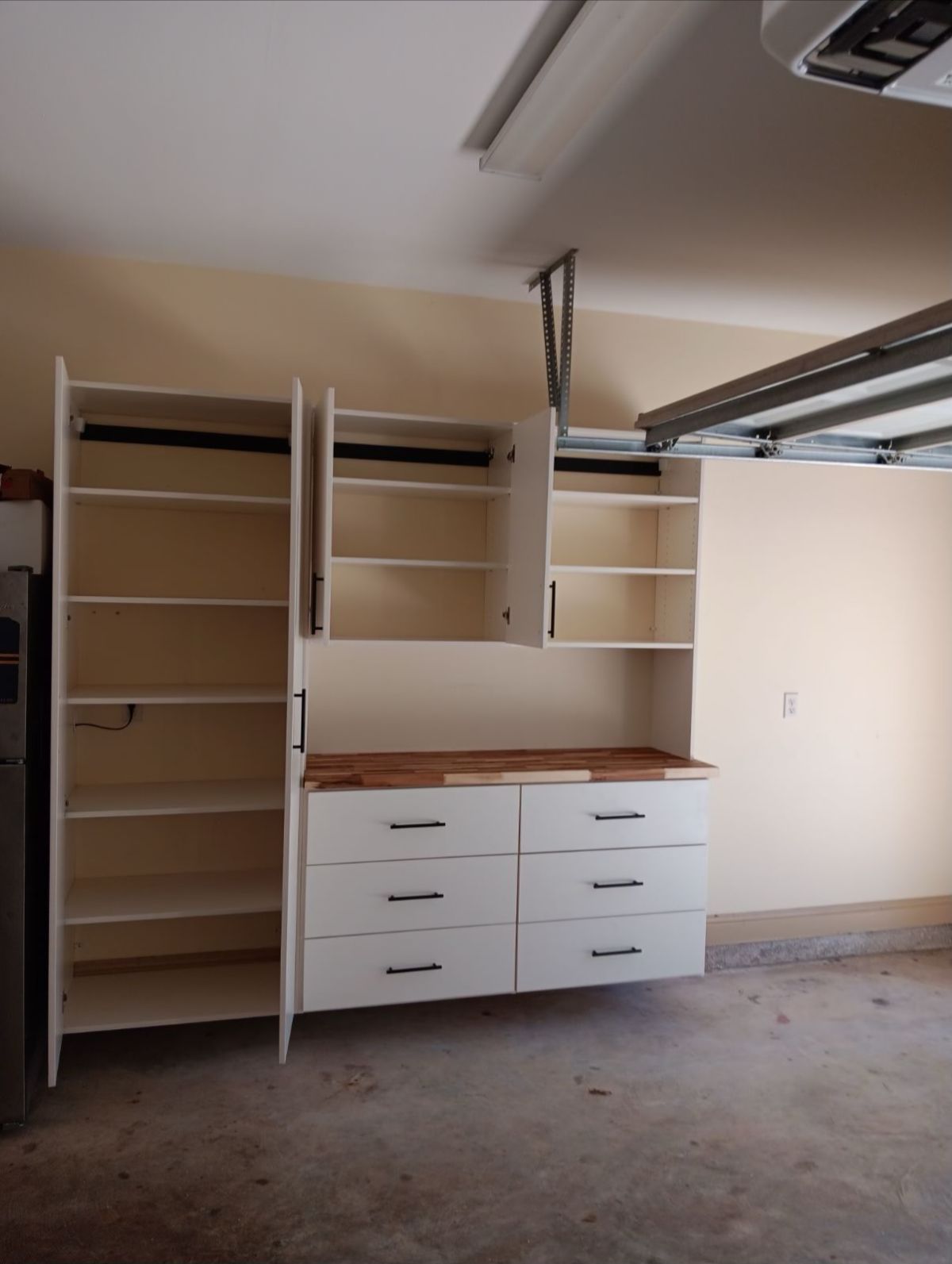 Garage cabinets with shelves, drawers, and open doors; beige and white against a light brown floor.