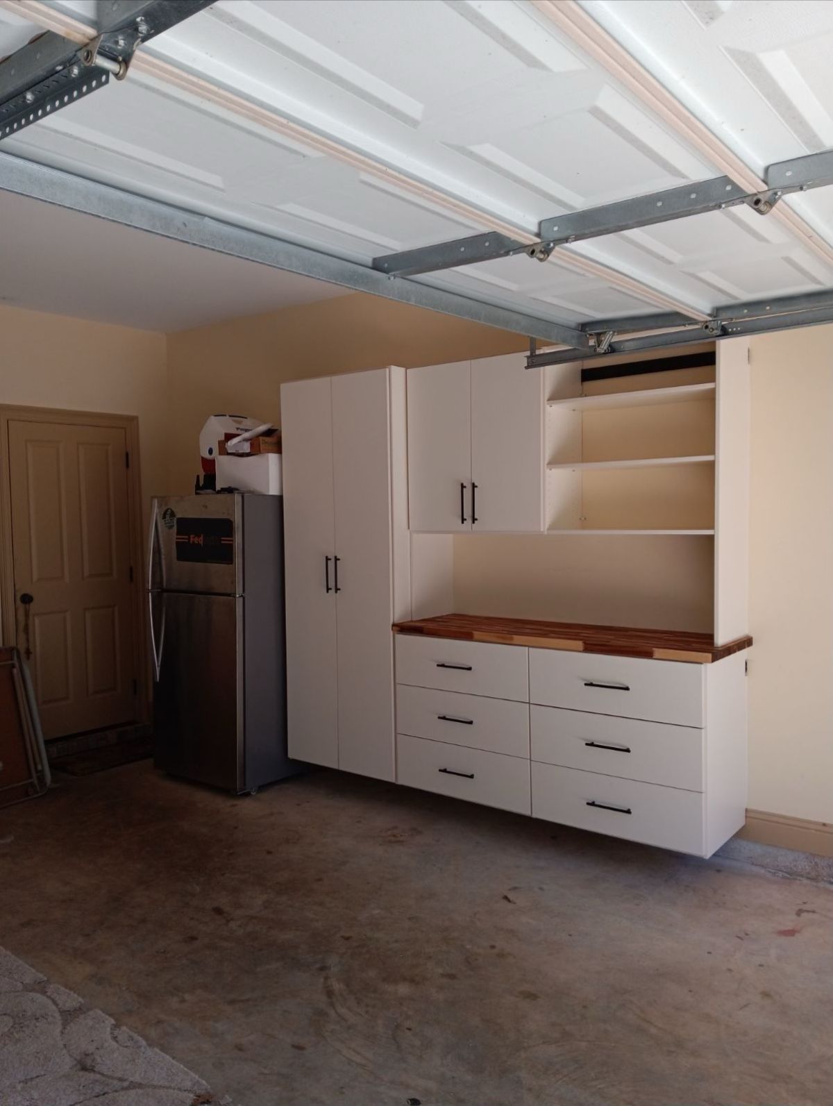 Garage interior with white cabinets, stainless steel refrigerator, and a wooden countertop.