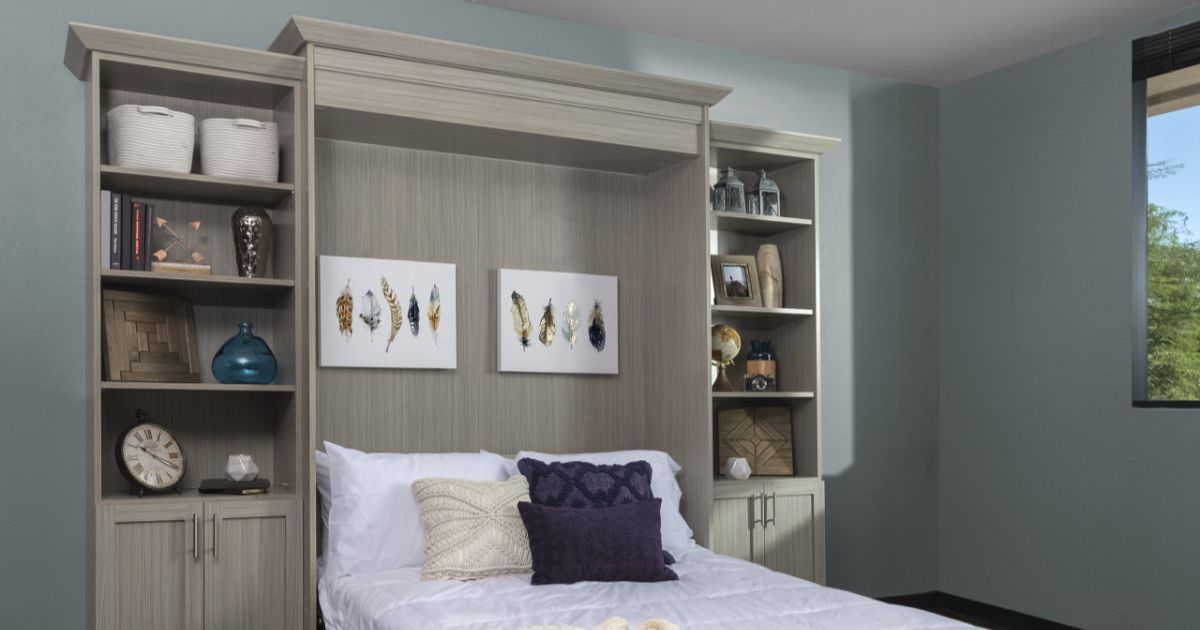 Built-in bed unit with shelves, framed art, and decorative pillows against a light blue wall.