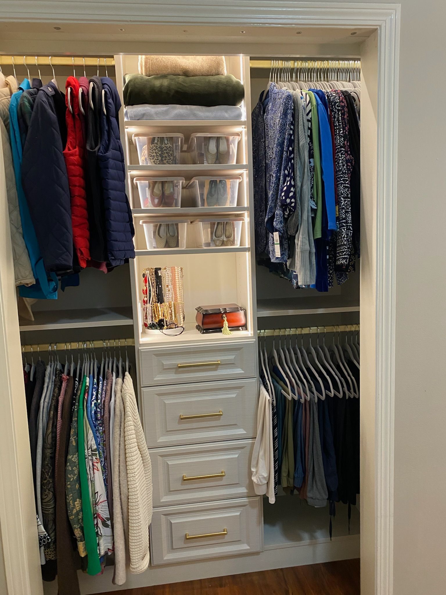 Custom closet with organized clothing, drawers, and shelving. White and gold accents.