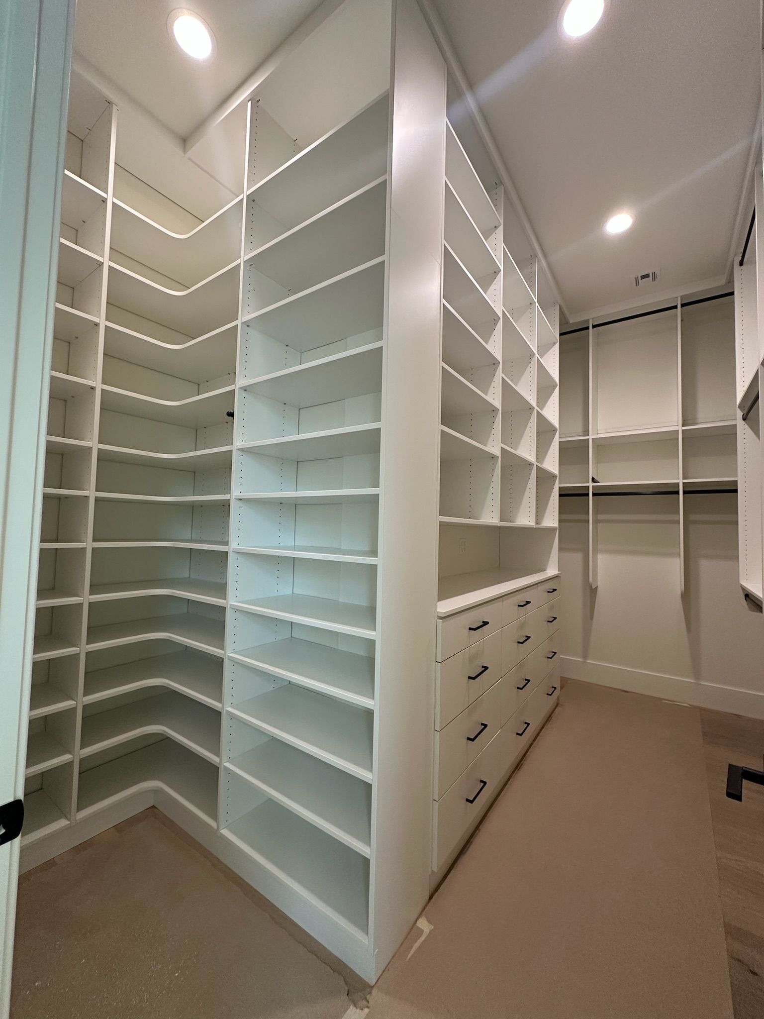 White walk-in closet with shelves and drawers. Beige carpet and bright overhead lights.