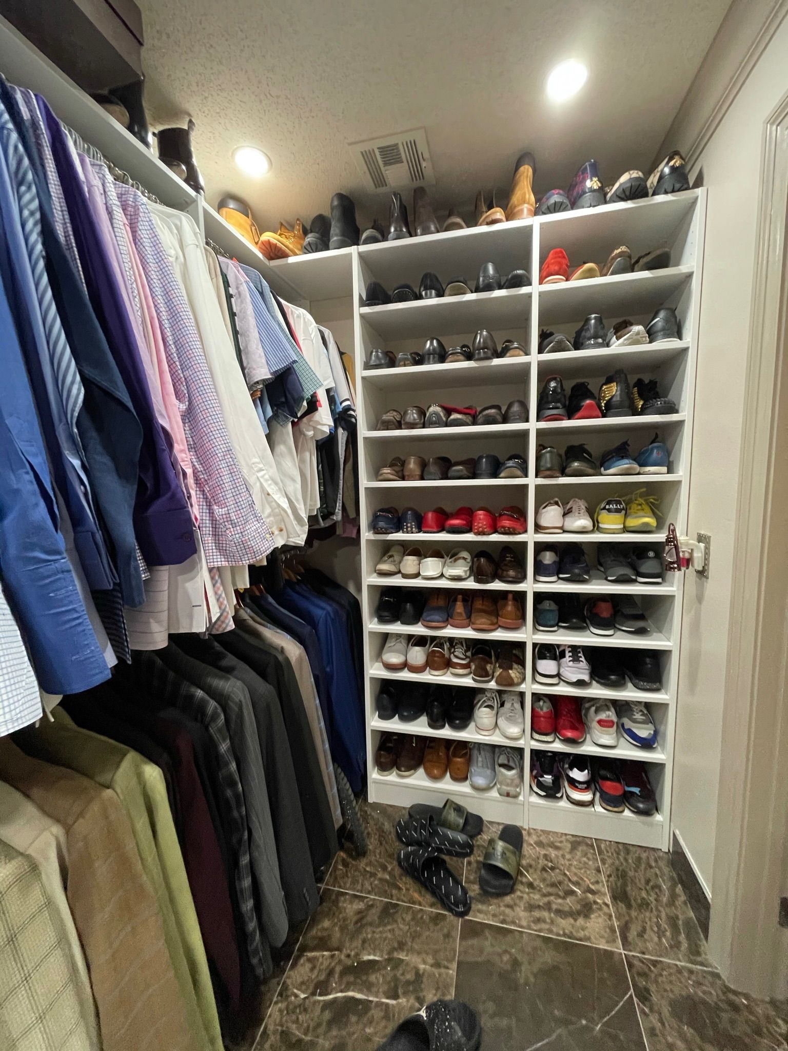 Walk-in closet with shirts and jackets hanging on the left, shoes on shelves to the right.