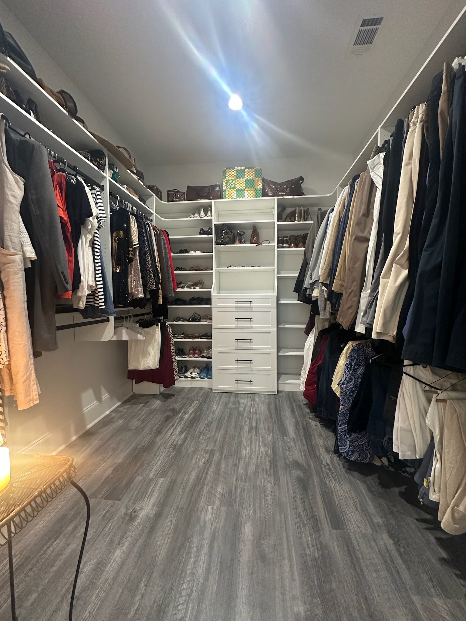 Walk-in closet with gray flooring, white shelves filled with clothes and shoes, and a central cabinet with drawers.