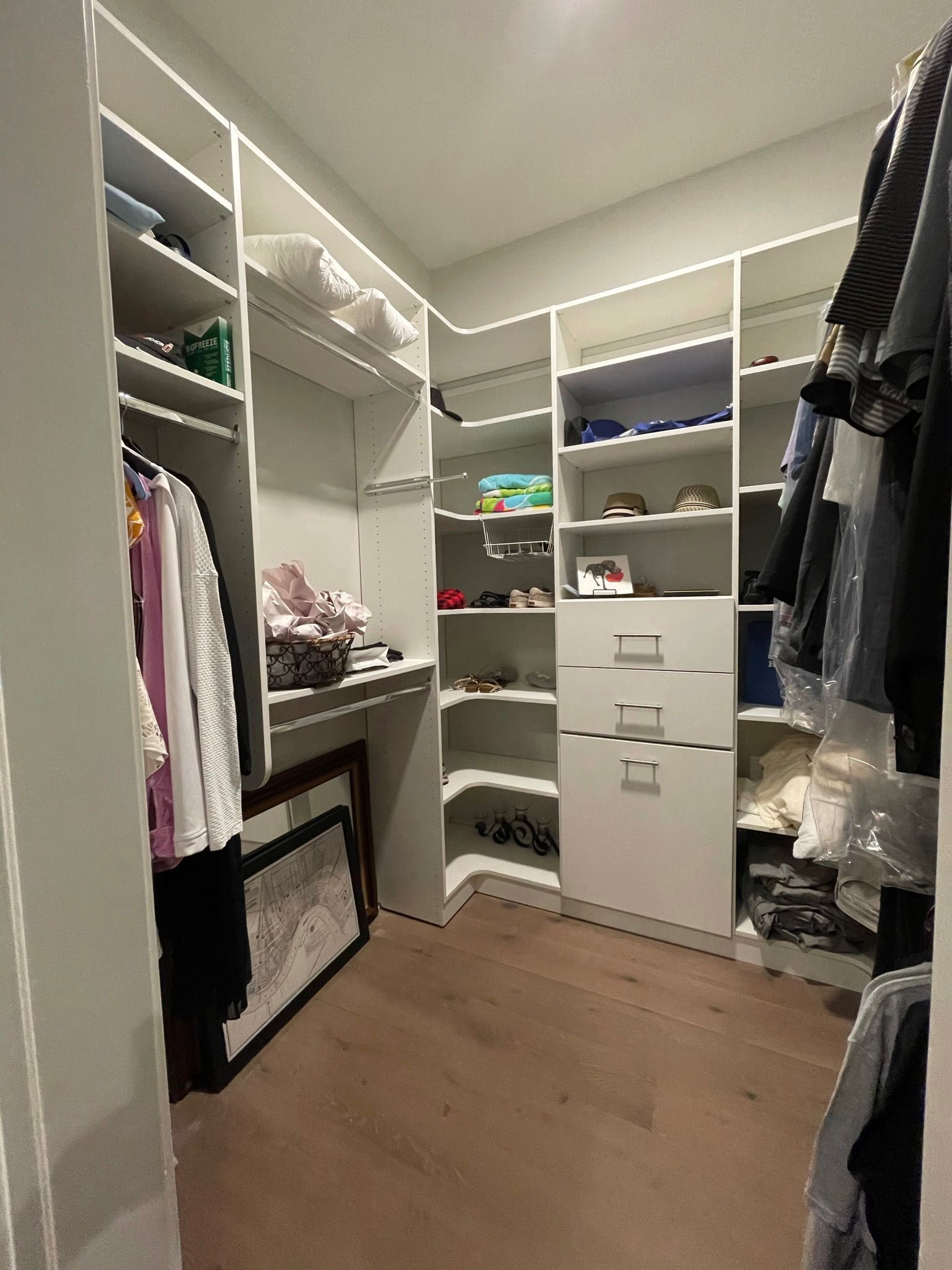 Walk-in closet with white shelving, wooden floor, and clothes hanging.