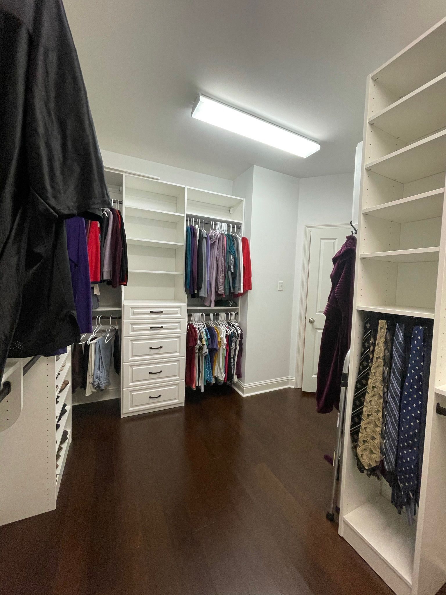 Walk-in closet with white shelving, dark wooden floor, and clothes hanging.