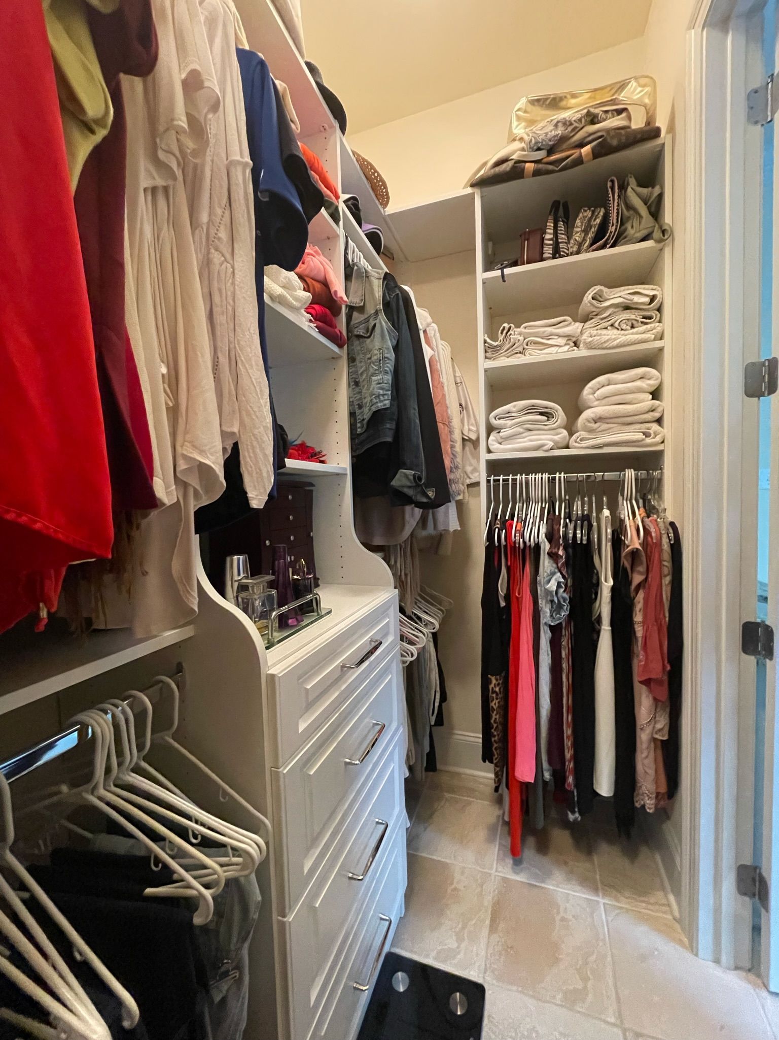 Walk-in closet with white shelves and drawers, filled with clothing and accessories.