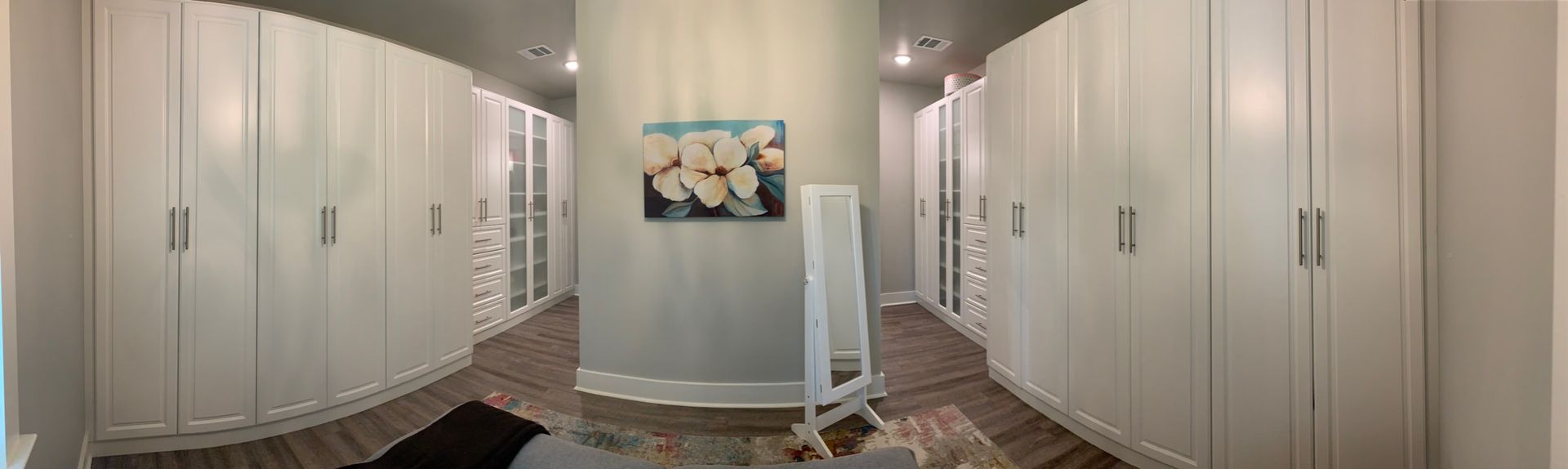 White walk-in closet with built-in cabinetry, mirror, and artwork on a light-colored wall.