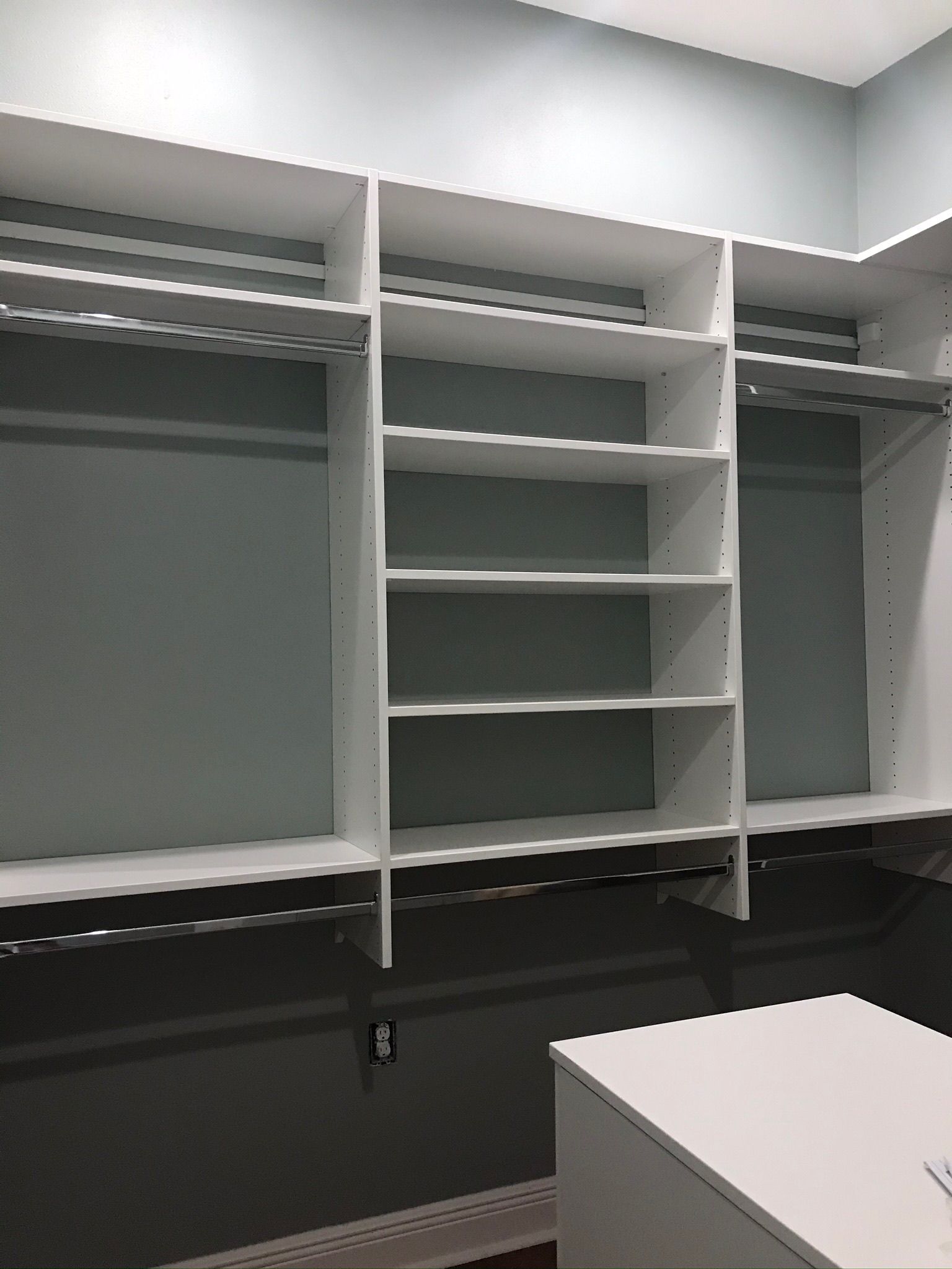 Empty white closet with shelves and hanging rods against gray and blue walls.
