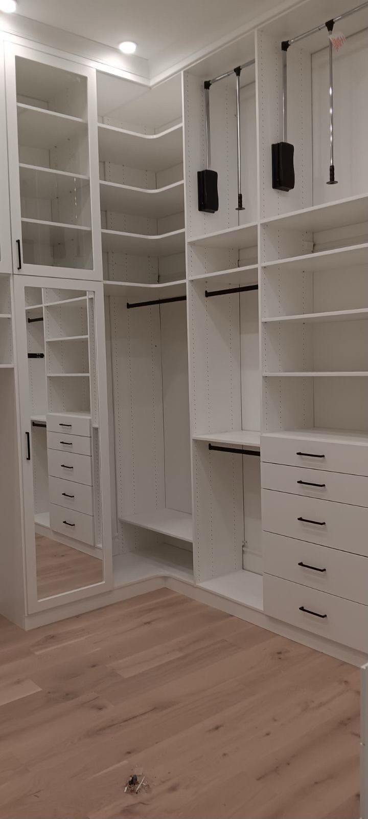 White custom closet with shelves, drawers, and hanging rods. Hardwood floor.