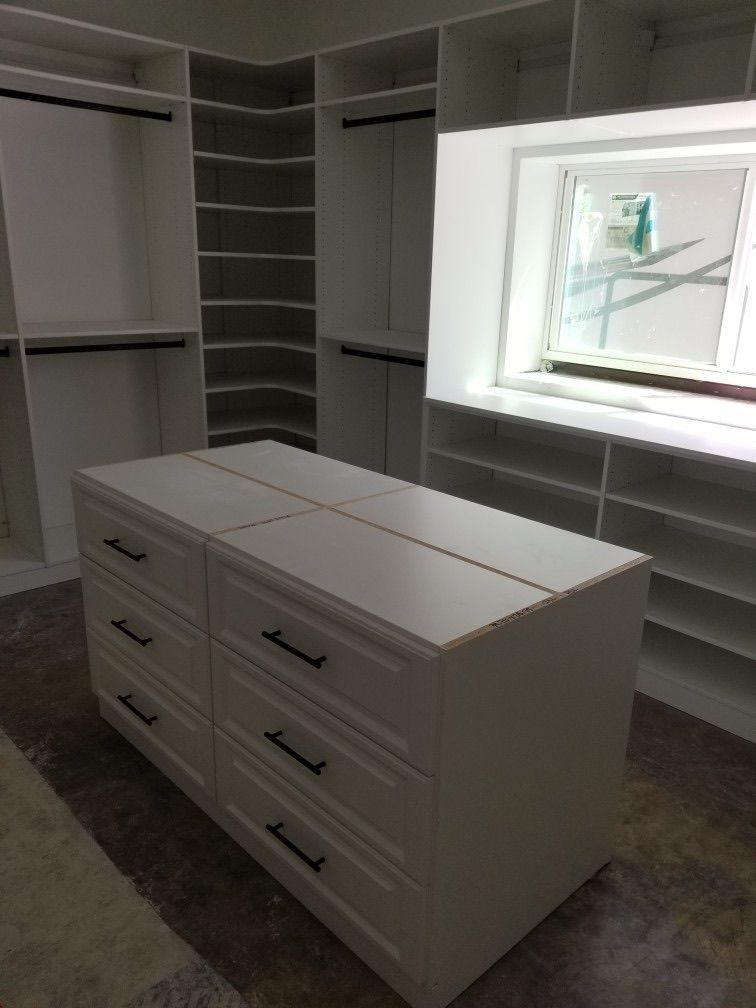 White closet with drawers, shelves, and hanging rods. Includes a center island and a window.
