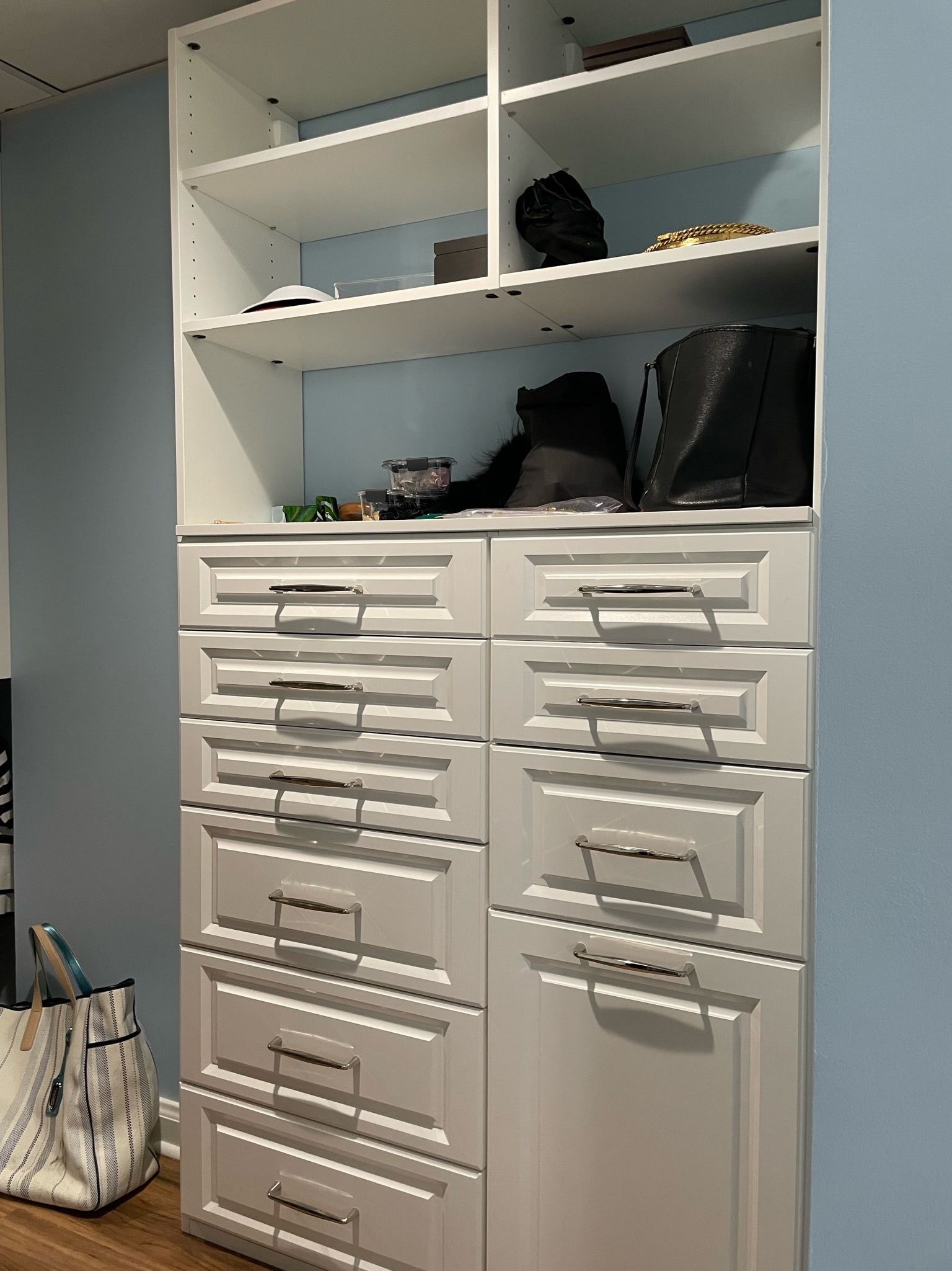 White closet with shelves and drawers against a light blue wall. A purse sits in front.