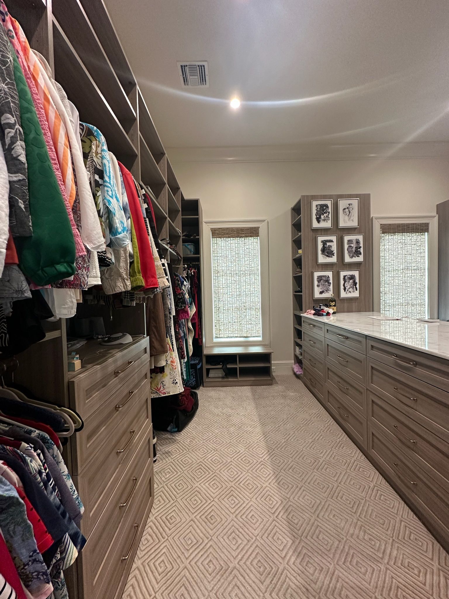 Walk-in closet with hanging clothes, drawers, shoe storage, and a center island, neutral colors.