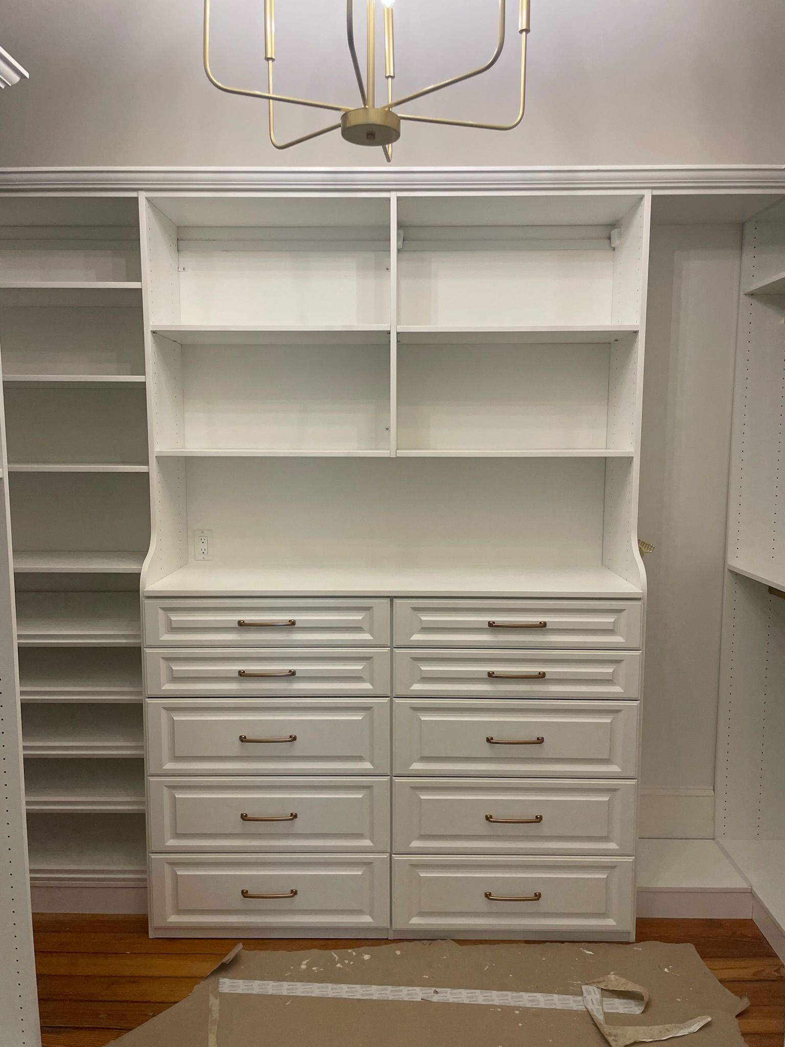 White closet organizer with drawers and shelves; gold chandelier in the ceiling above.