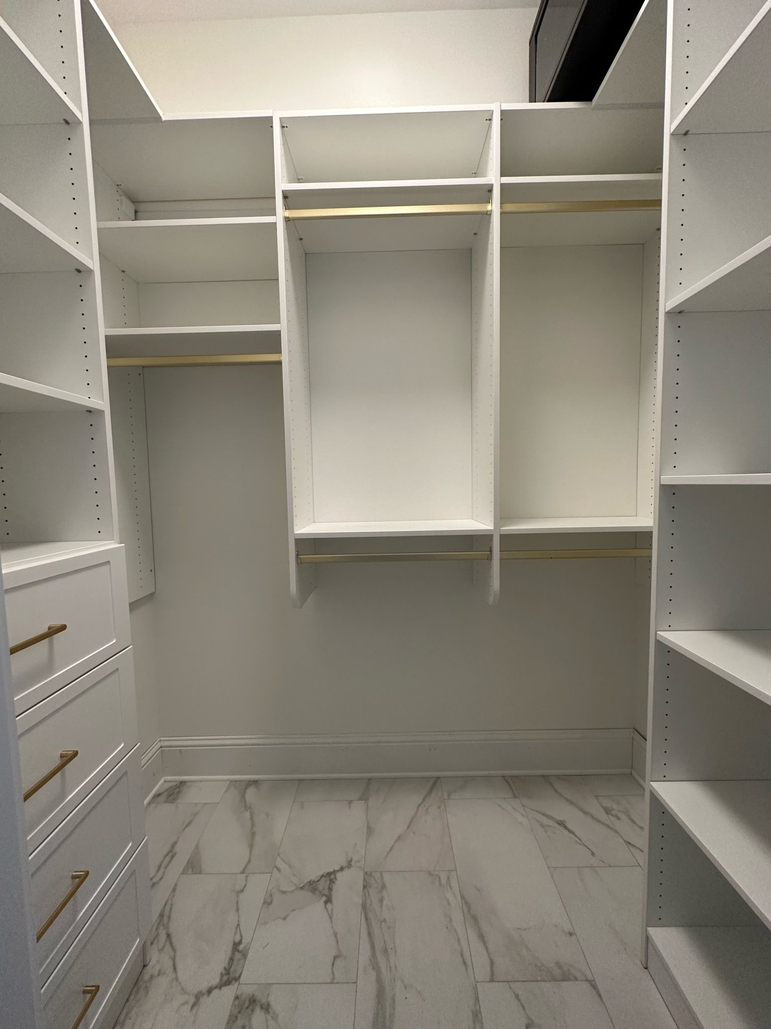 Empty white walk-in closet with shelves, hanging rods, and a marble-tiled floor.